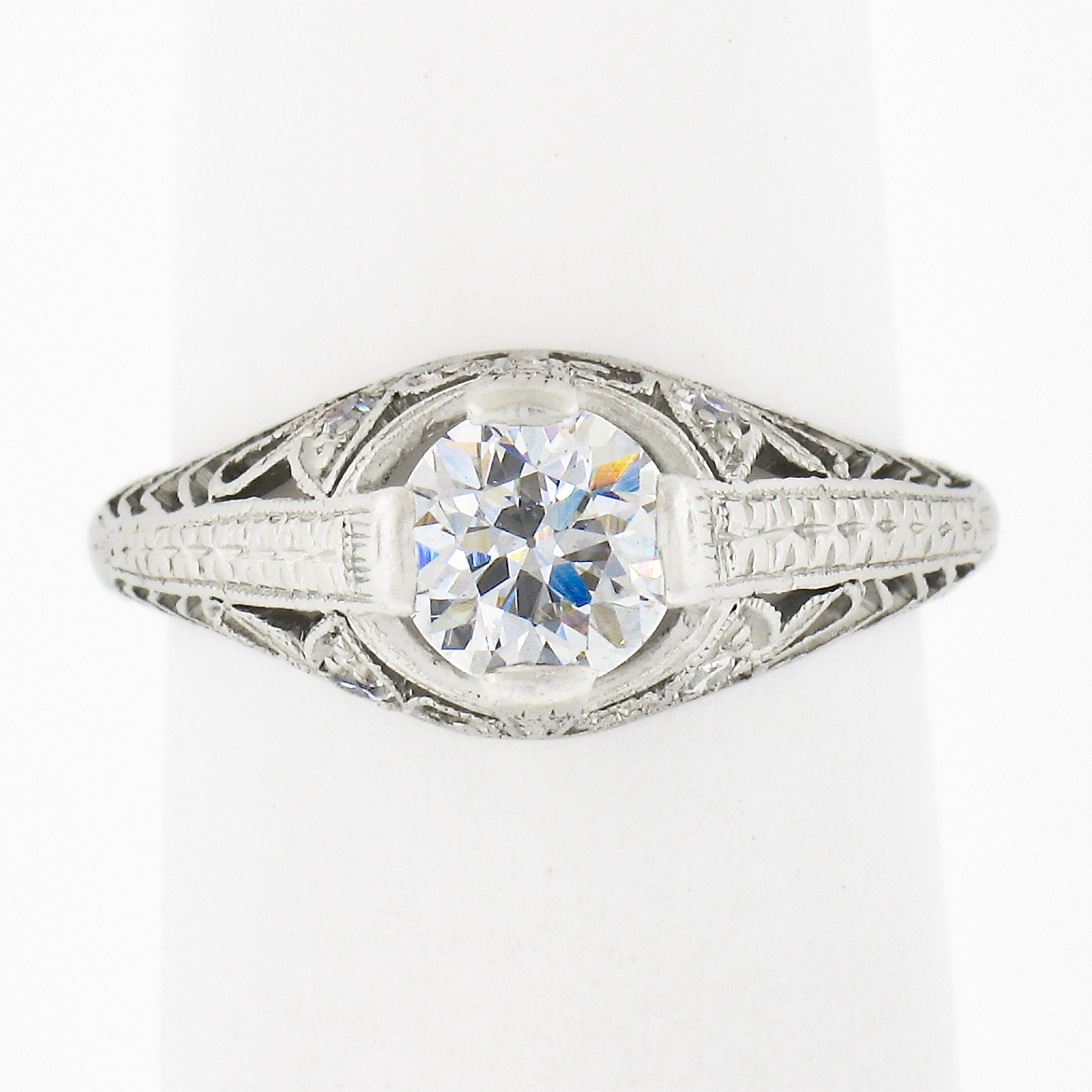 This incredible antique diamond solitaire ring was crafted in platinum during the edwardian period and features a slightly puffed top that is decorated with open filigree work and floral patterns, while the shank showcases wonderful wheat engraving