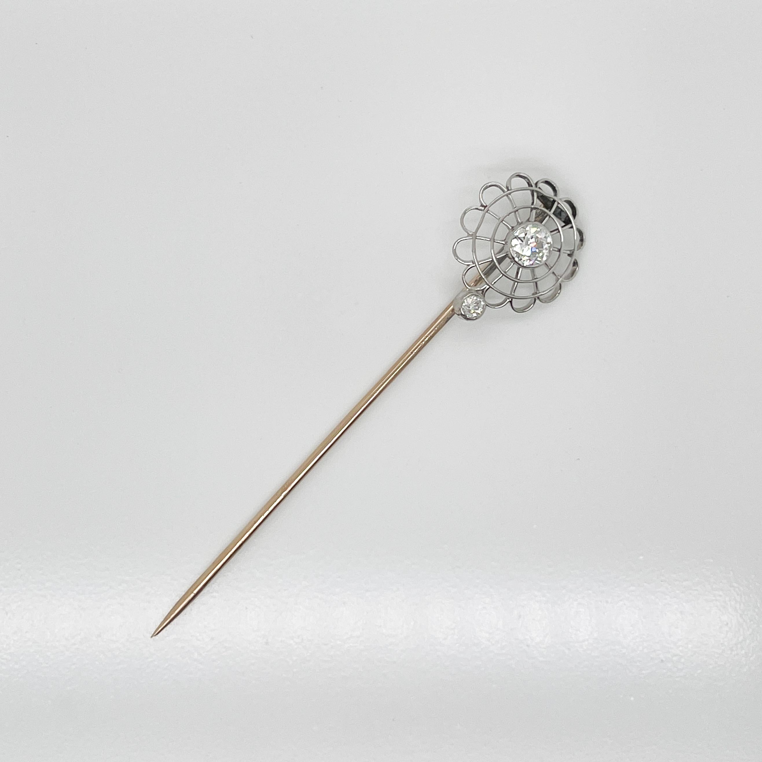 A very fine Edwardian stick pin.

In a platinum spider web (or stylized flower) pattern.

With a bezel set diamond in center and bottom of wire frame.  

Mounted on a 10k gold pin stem.

A great stick pin!

Date:
Early 20th Century

Overall