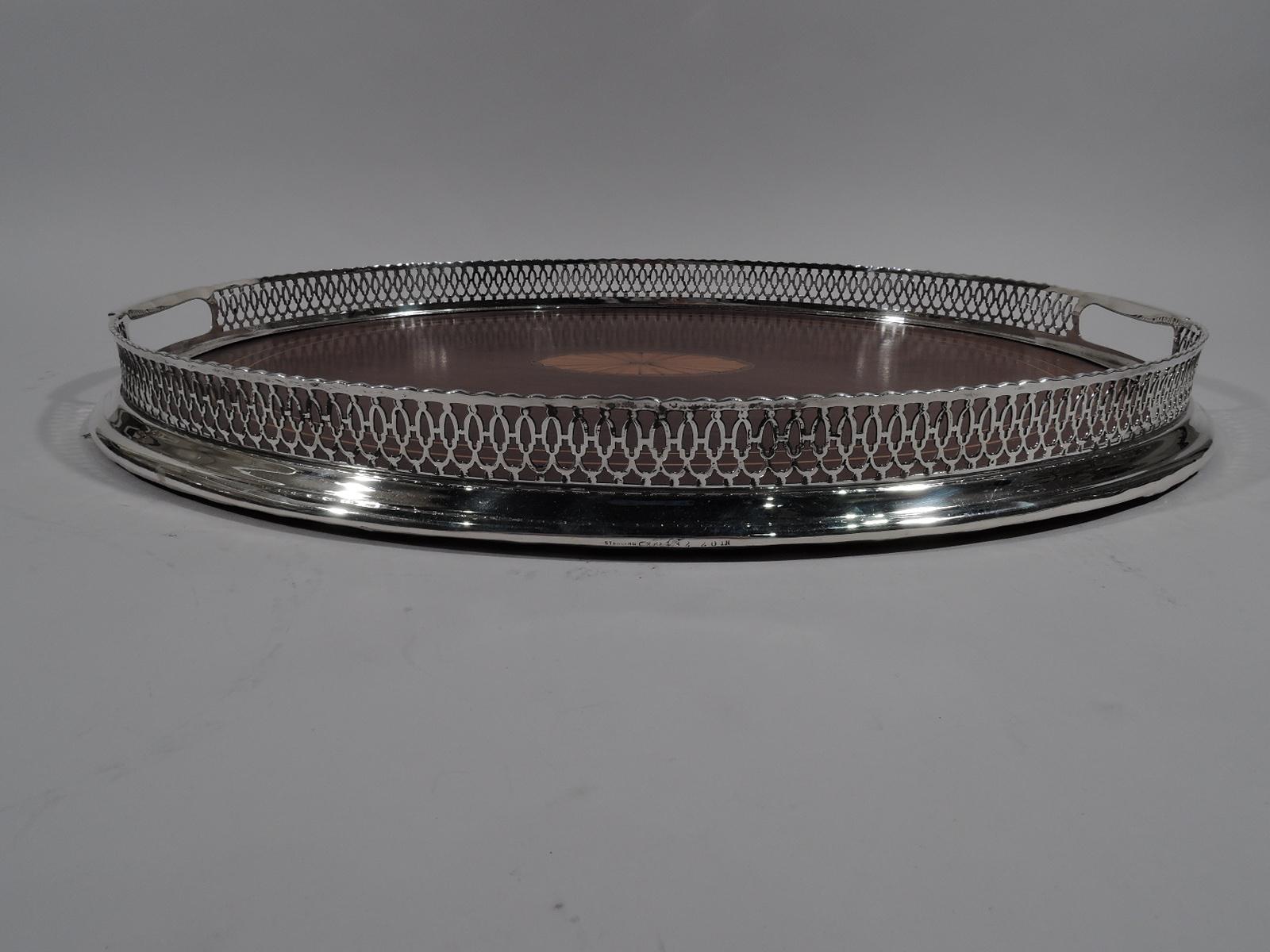 Edwardian tea tray. Made by Dominick & Haff in New York, circa 1910. Oval stained-wood well with marquetry patera and 2 linear borders set in sterling silver frame with pierced geometric gallery sides and spread base. Tubular cutout end handles with