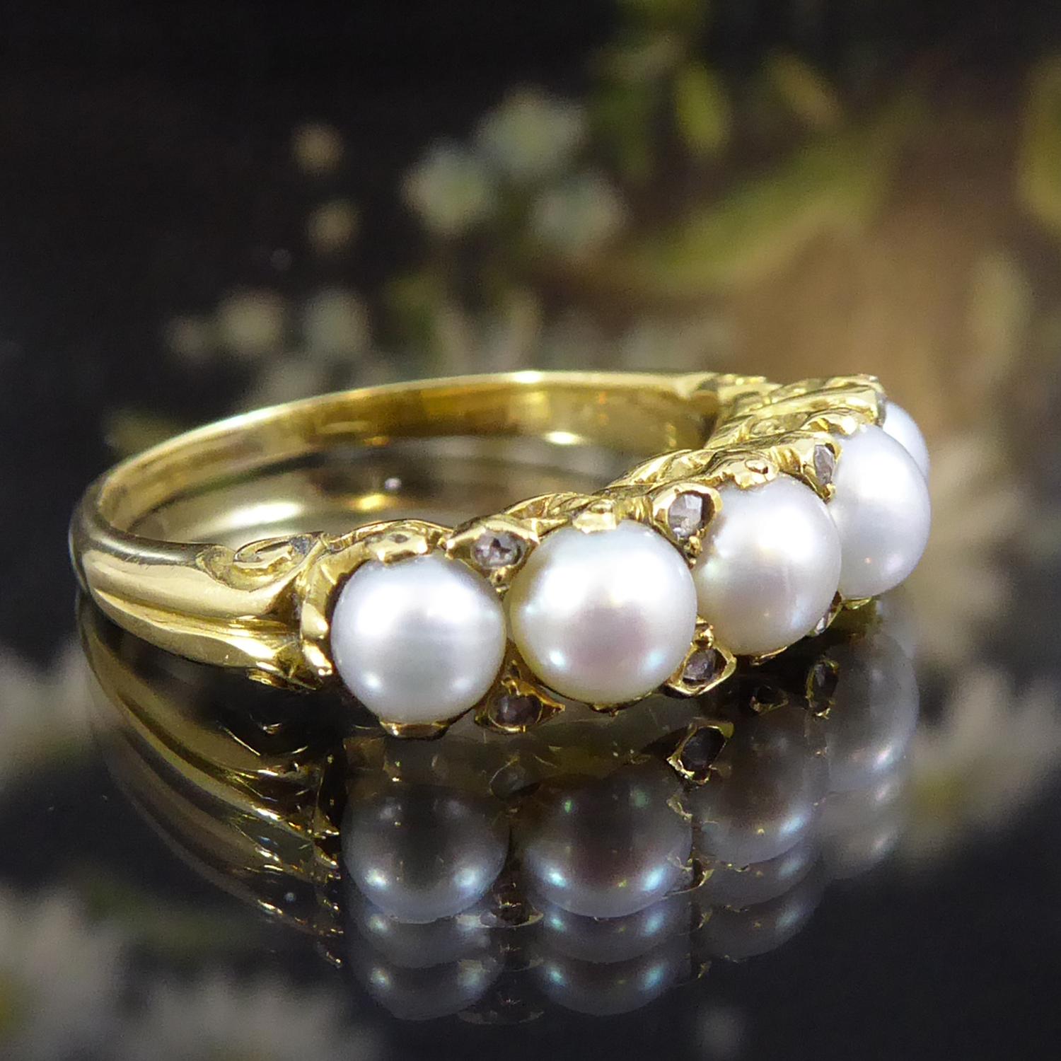 A stunnning five stone ring from the Edwardian era circa 1900s comprising five round creamy white pearls in a row across the finger.  The pearls are claw set to a decorative yellow gold  gallery and in the space between each pearl, to either edge of