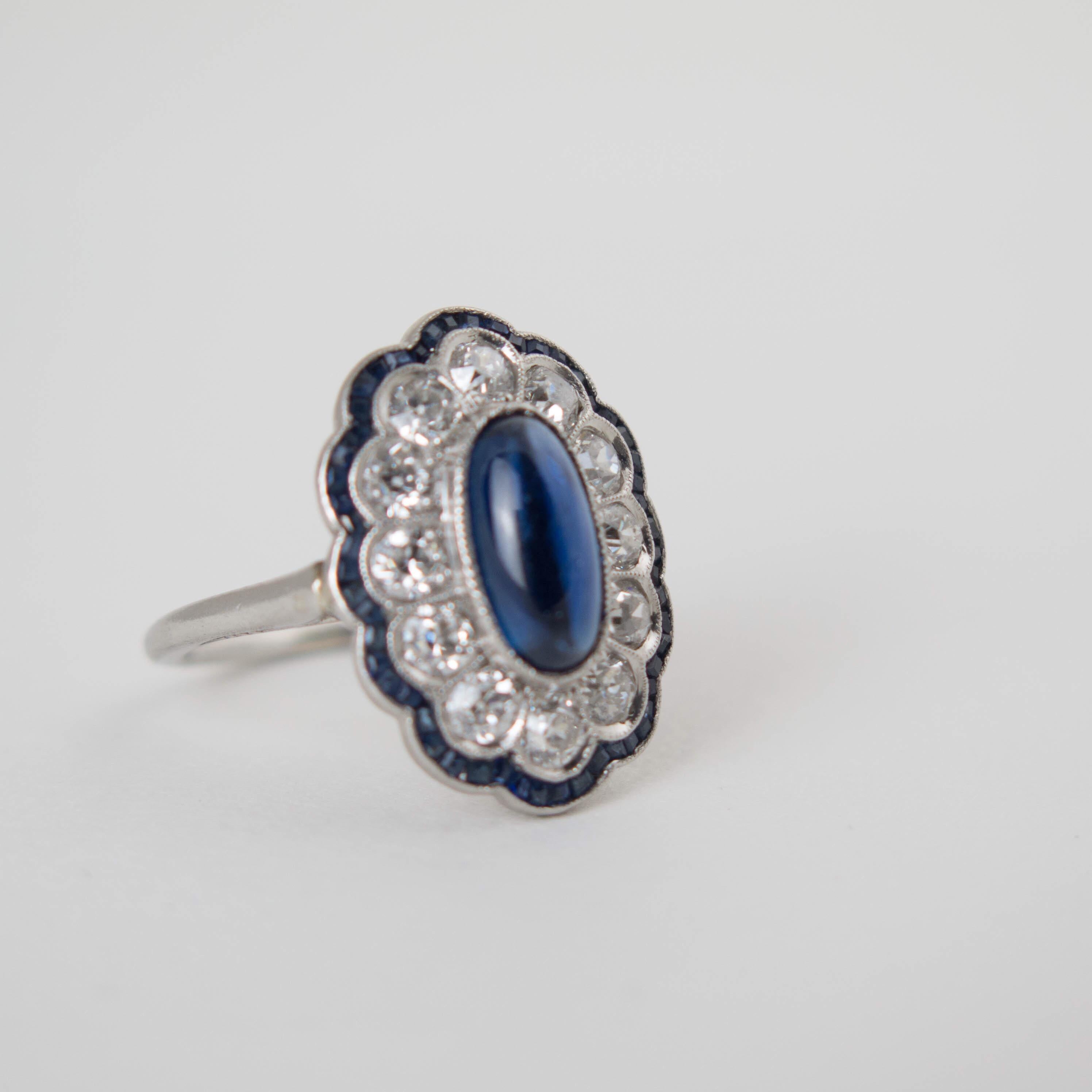 An exquisite and charming Edwardian sapphire and diamond engagement ring set in platinum. 

The early 20th century Edwardian platinum ring is centered around a luscious long and tall natural blue sapphire cabochon. The central sapphire is surrounded