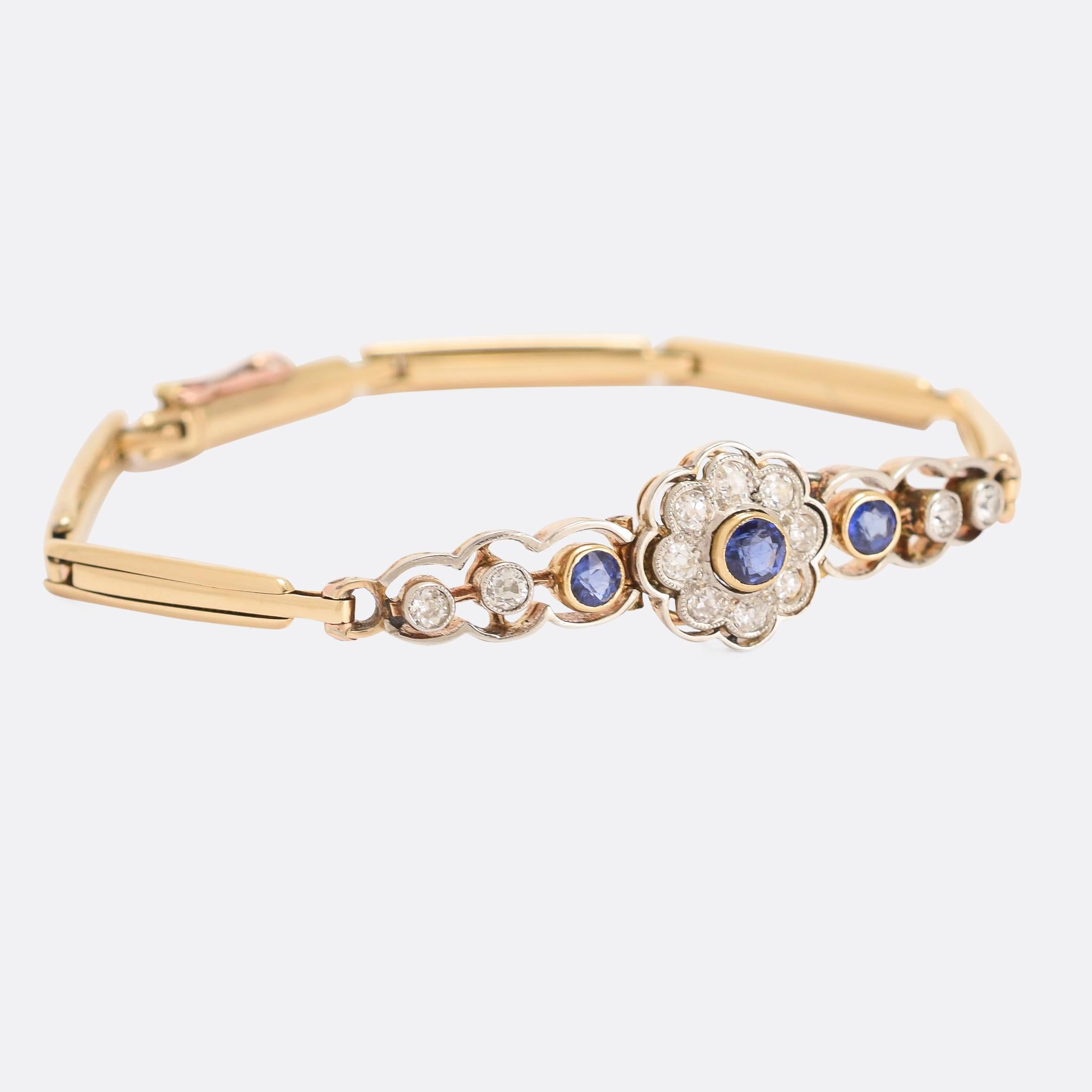 A simple and refined Edwardian bracelet set with vibrant blue sapphires and old cut diamonds. The centrepiece is a gemset daisy, flanked by three stones on either side, and all within a platinum halo. The links are sprung to keep it flush against