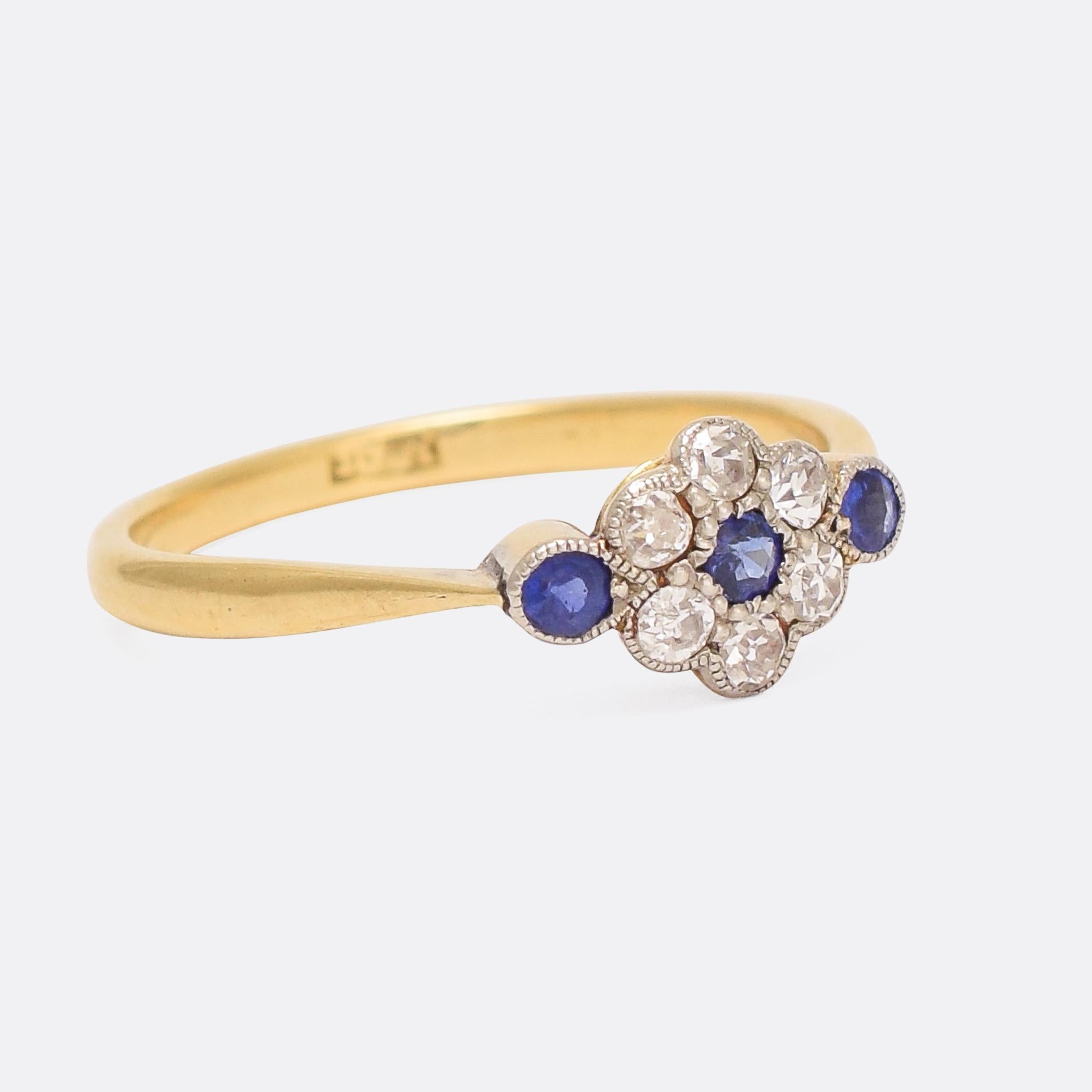 A sweet antique cluster ring with sapphires and diamonds millegrain platinum settings. The head features a central daisy, flanked by two sapphires in teardrop settings. The simple band joins the head with elegant pinched shoulders; it's modelled in