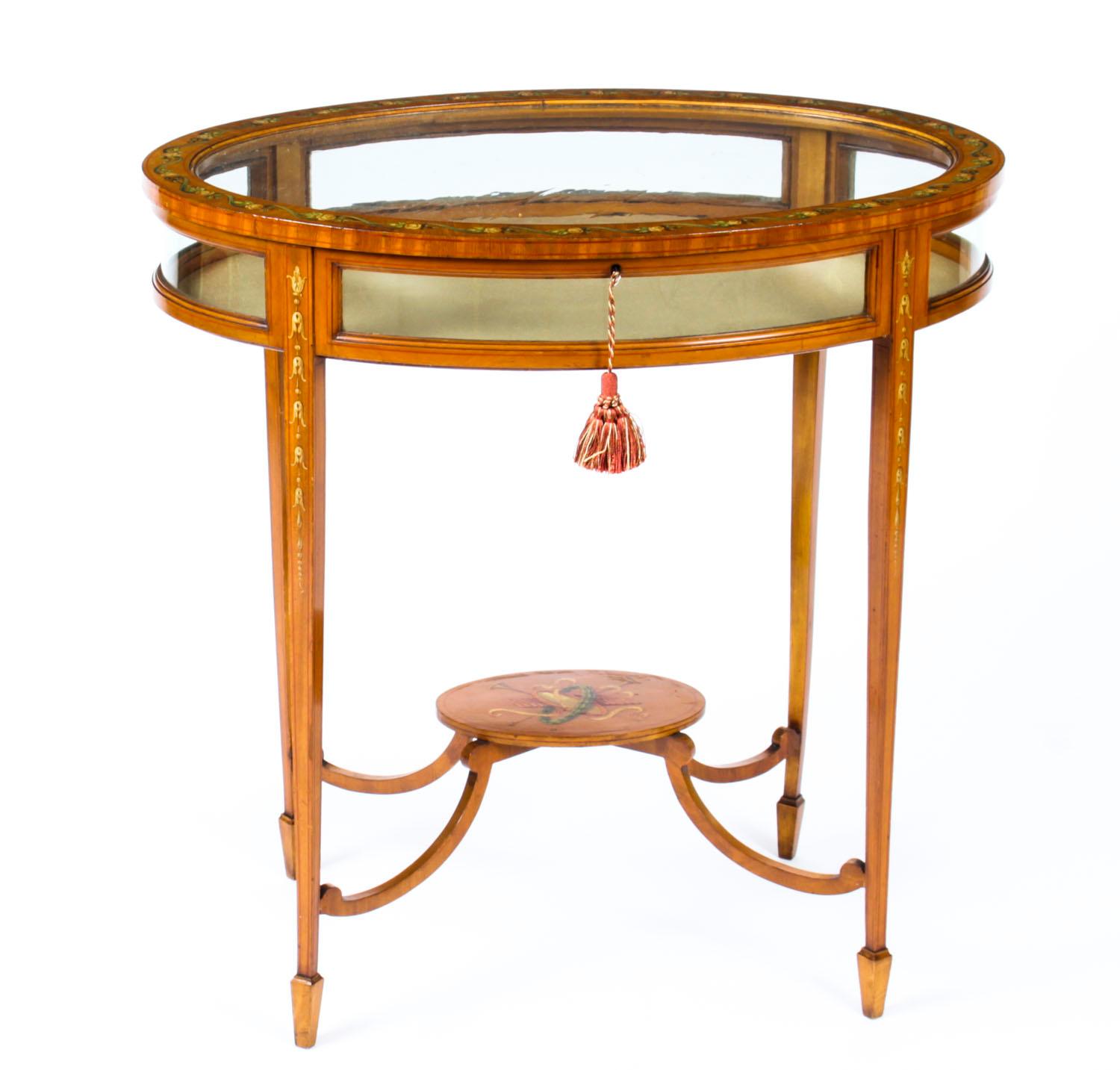 This is a truly beautiful antique Edwardian Satinwood bijouterie display table circa 1900 in date.
 
The oval shaped display table has a hinged glazed lid decorate and it is raised on square tapering legs joined by an oval under-tier decorated with