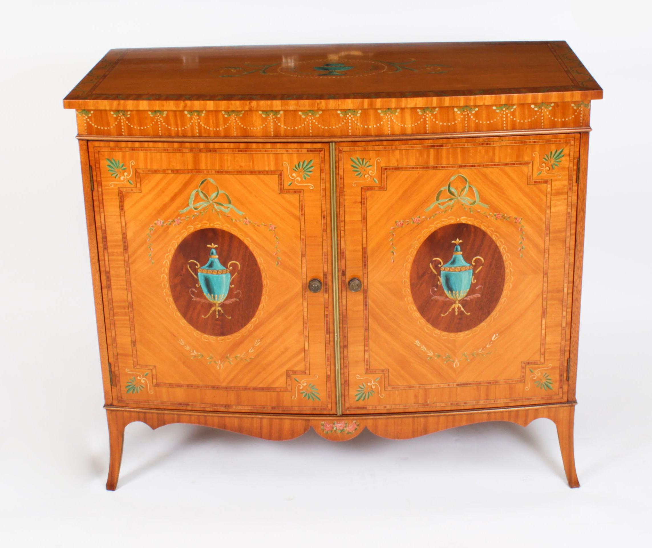 This is a stylish English Edwardian satinwood, hand-painted and wood banded bowfront side cabinet, circa 1900 in date.
 
This splendid cabinet is made of the finest quality satinwood and hand painted in the manner of Angelica Kauffman. The top is
