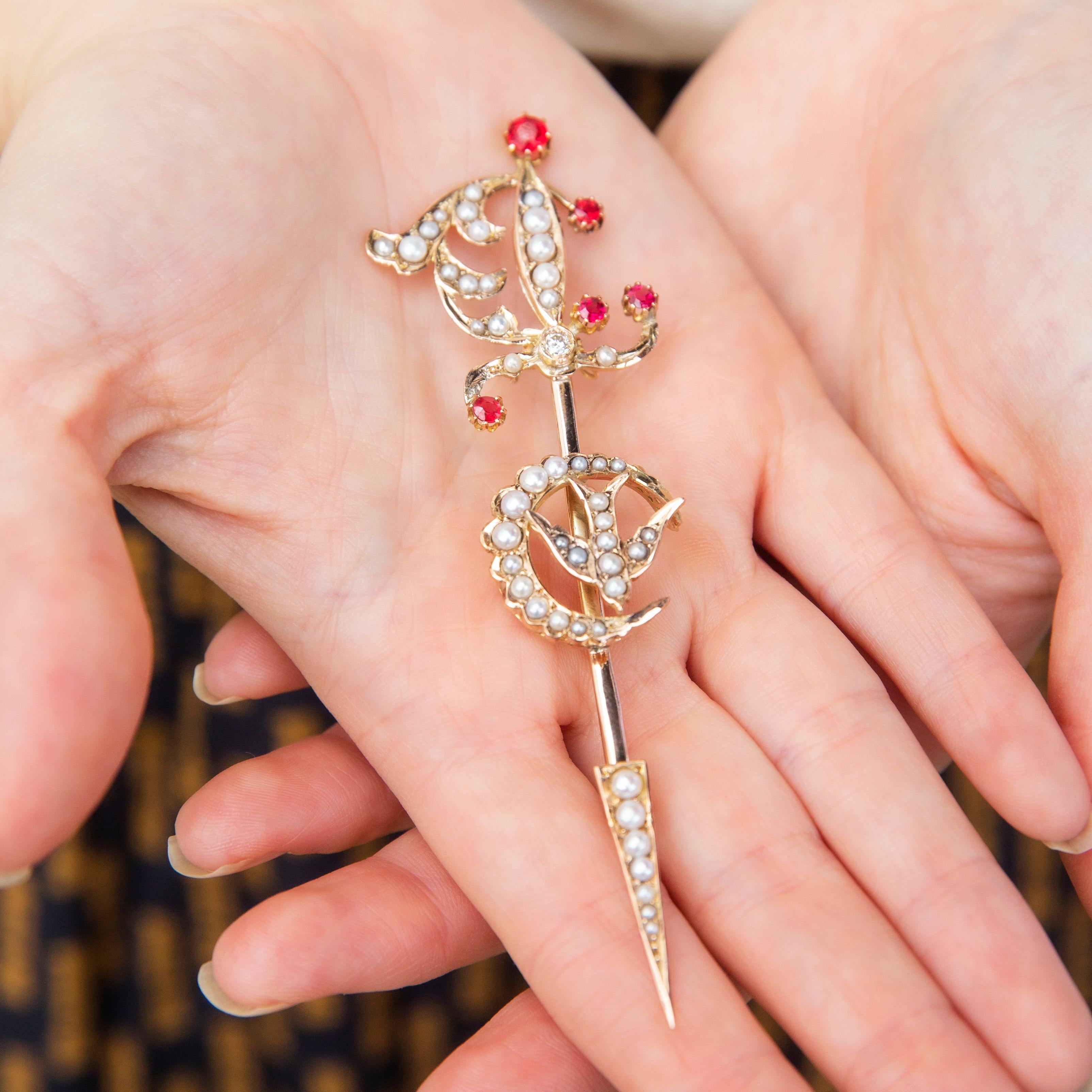 Imprégnée de l'histoire édouardienne, la broche Mary est exquise. L'épée, le croissant de lune et l'hirondelle sont magnifiquement travaillés en or 9 carats. Des rubis cramoisis et de somptueuses perles de rocaille embellissent et adoucissent les