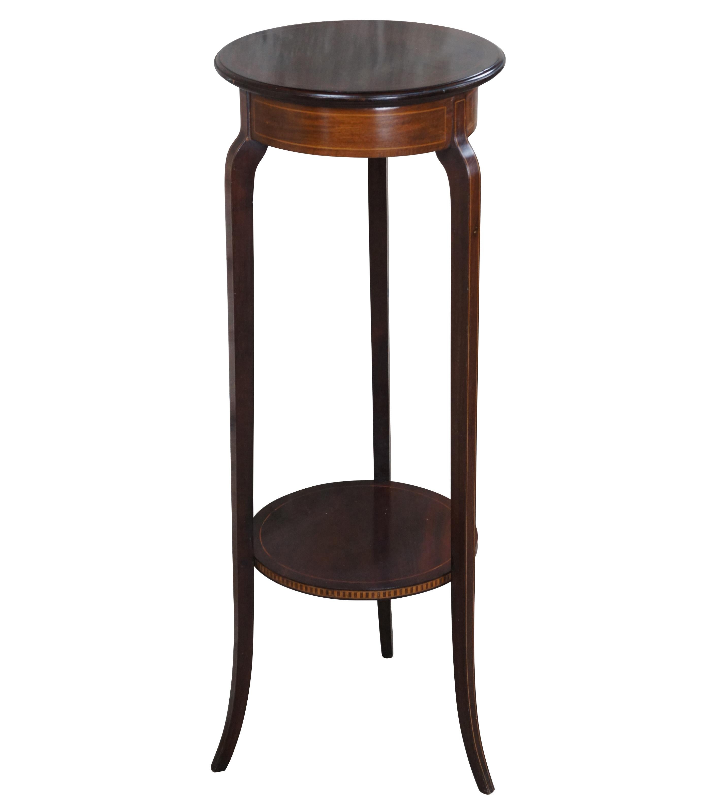 English Edwardian plant stand or sculpture pedestal, circa 1900-1910.  Made from Mahogany with satinwood inlay.  Features a round form over three slender legs connected towards the bottom by a banded shelf

Dimensions: 
36