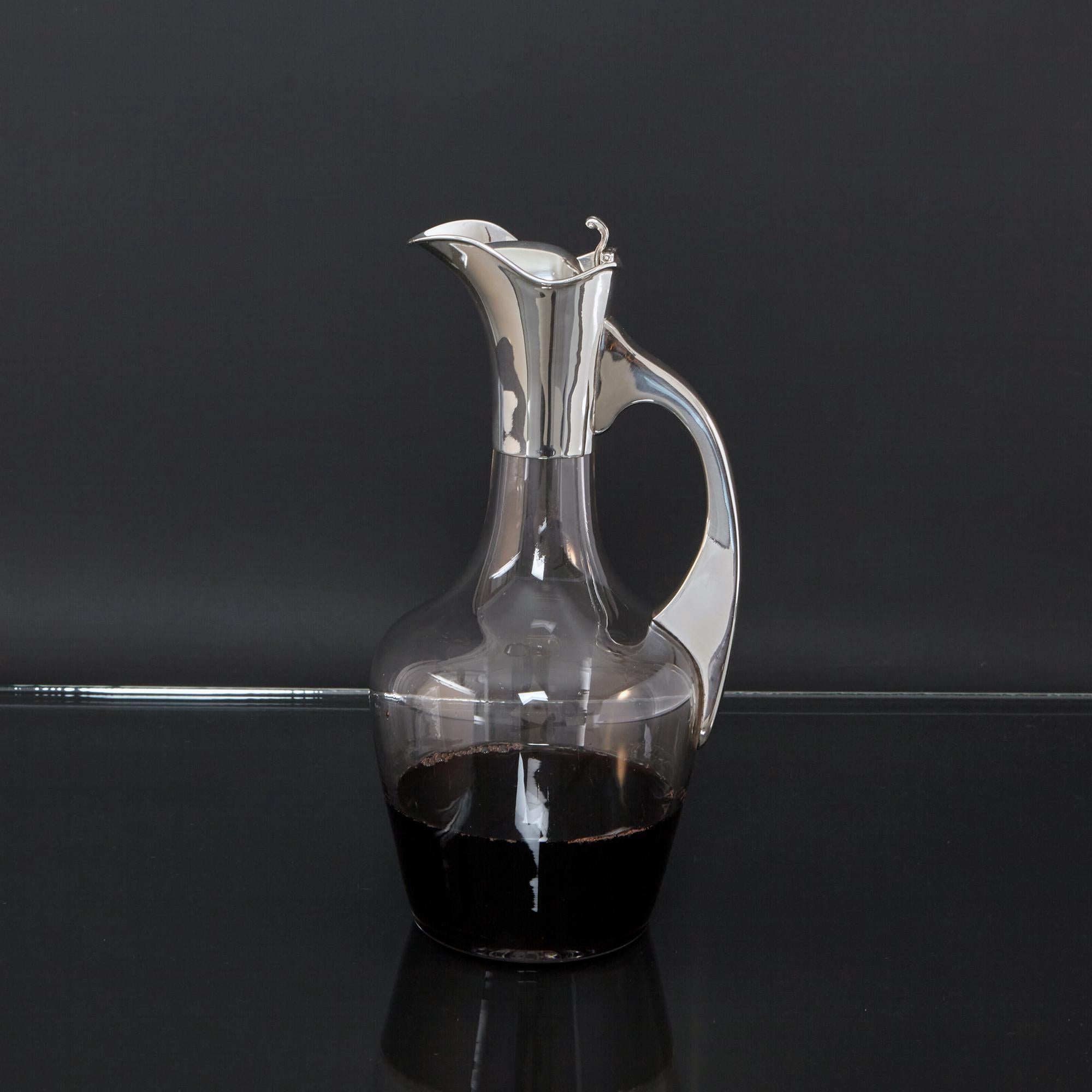 A graceful antique Arts Nouveau style silver and glass wine jug from the Edwardian period at the start of the 20th century. The hand-blown glass body is cut with a starburst pattern on the base, the silver collar, hinged domed cover and tapering