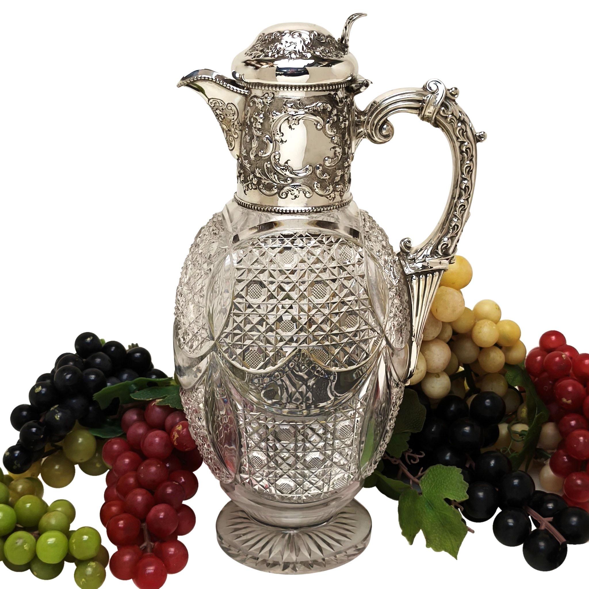Una bellissima caraffa Claret antica in argento sterling e vetro tagliato. Questa brocca da vino presenta un disegno a volute e fogliame sul collo e sul coperchio incernierato e ha una coppia di cartigli sui lati opposti del collo. La brocca Claret