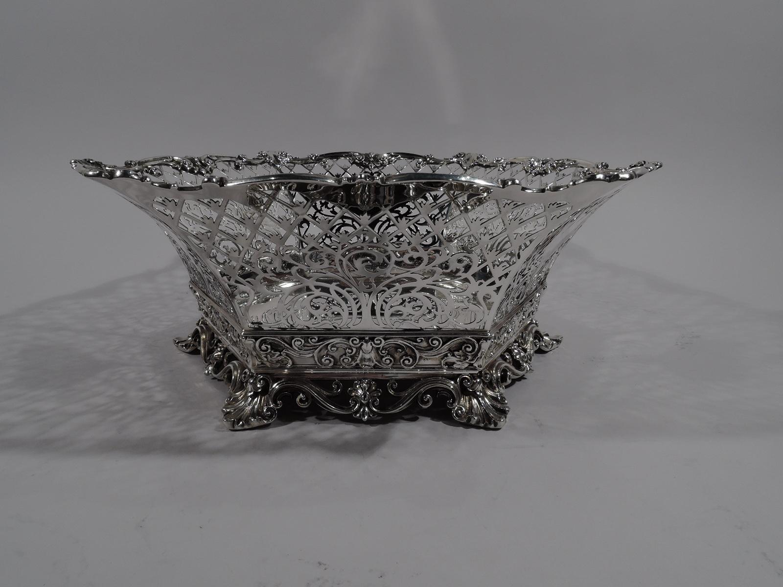 Edwardian sterling silver centerpiece basket bowl, 1898. Solid hexagonal well and tapering open trellis sides with fluid scrollwork and solid shaped cartouches (vacant). Sides have applied scrolls, leaves, and leaves. Solid border at bottom with