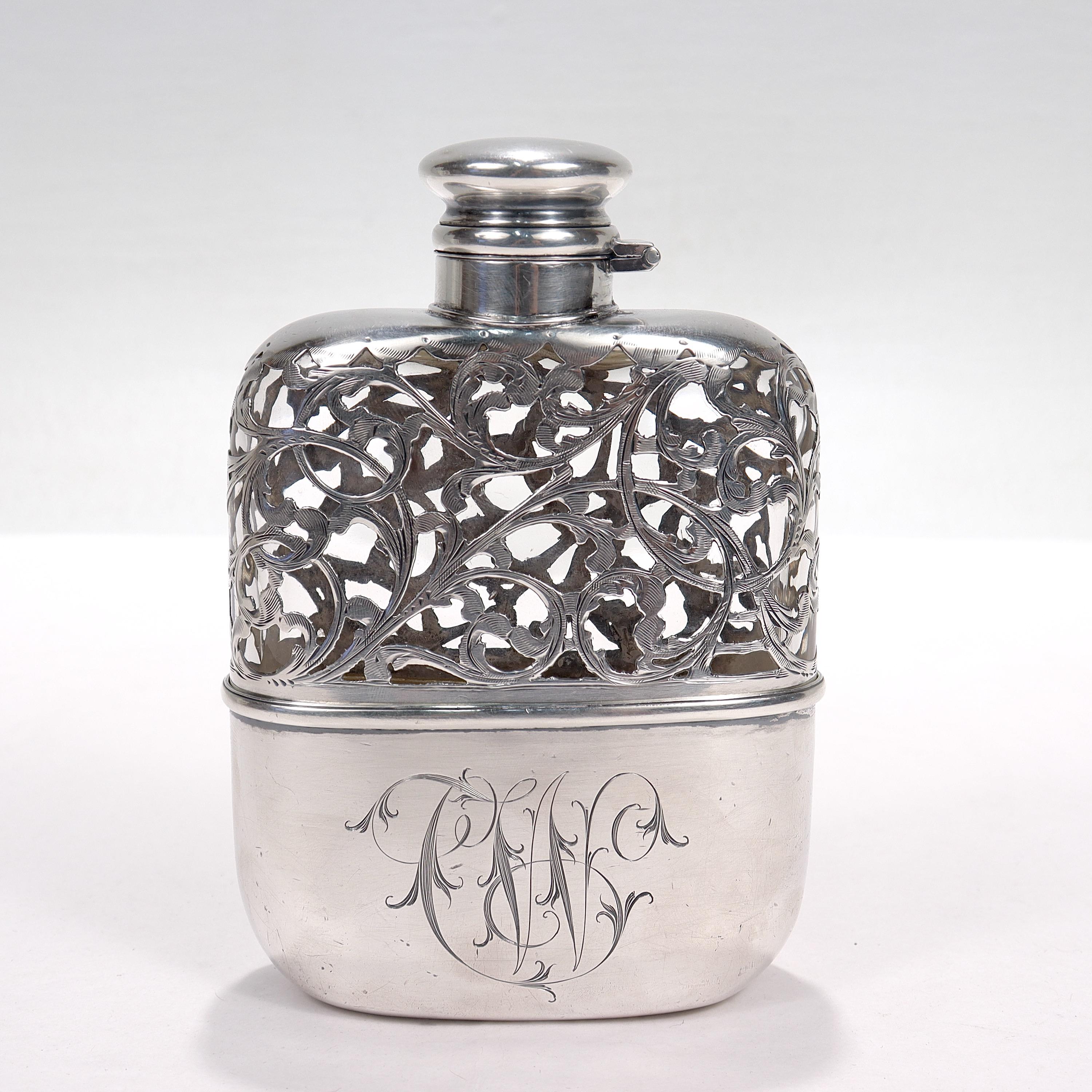 A fine antique hip flask.

In sterling silver and glass with a silver overlay top, a hinged, twist-top lid, and a removable cup to the base. 

Monogrammed with a cursive 