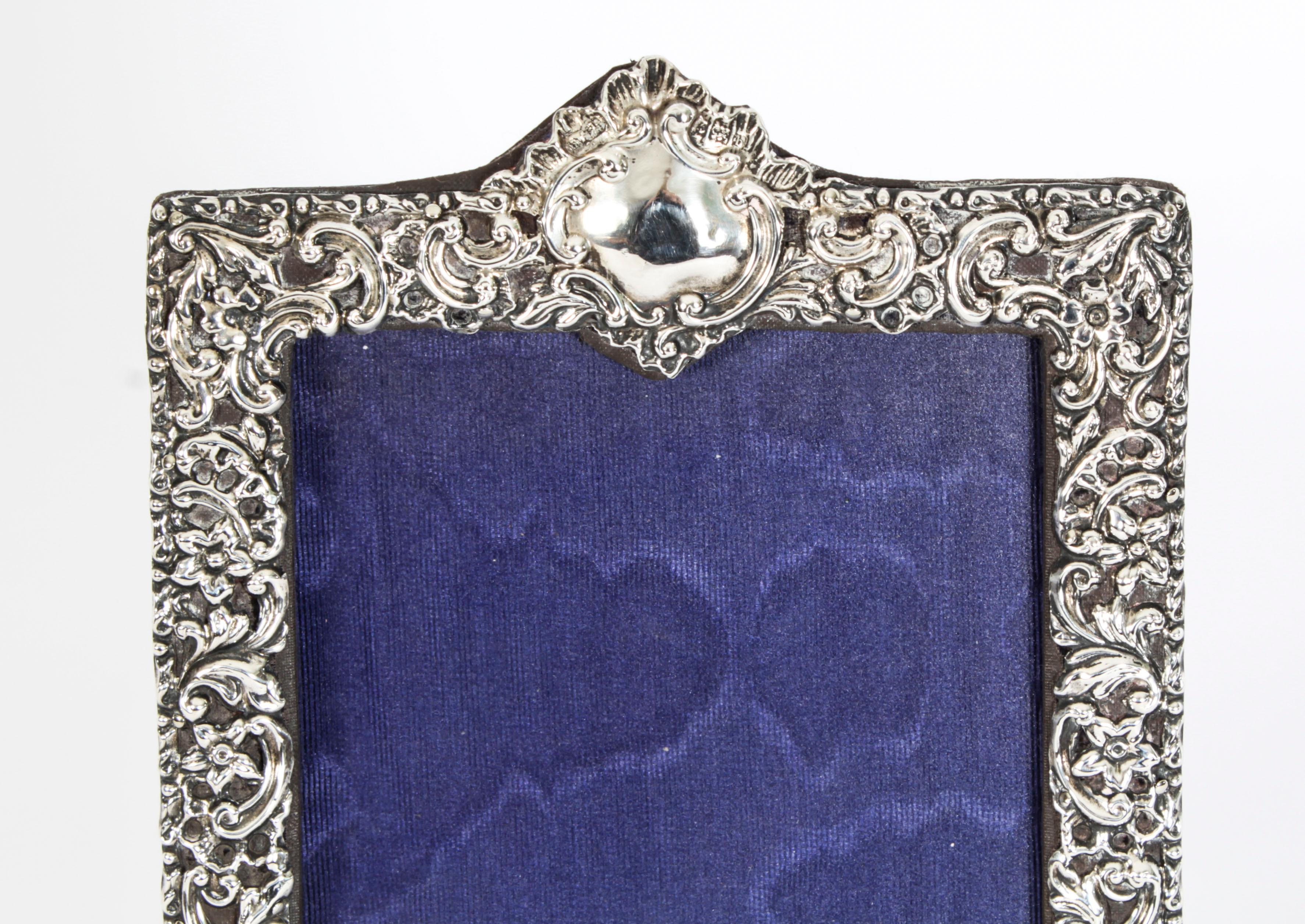 A pretty Edwardian sterling silver photograph frame having extensive cut decoration, plain cartouche and a blue leather bound easel back.
 
With hallmarks for Birmingham 1901.
 
Beautifully decorated portrait frame with floral and scroll relief