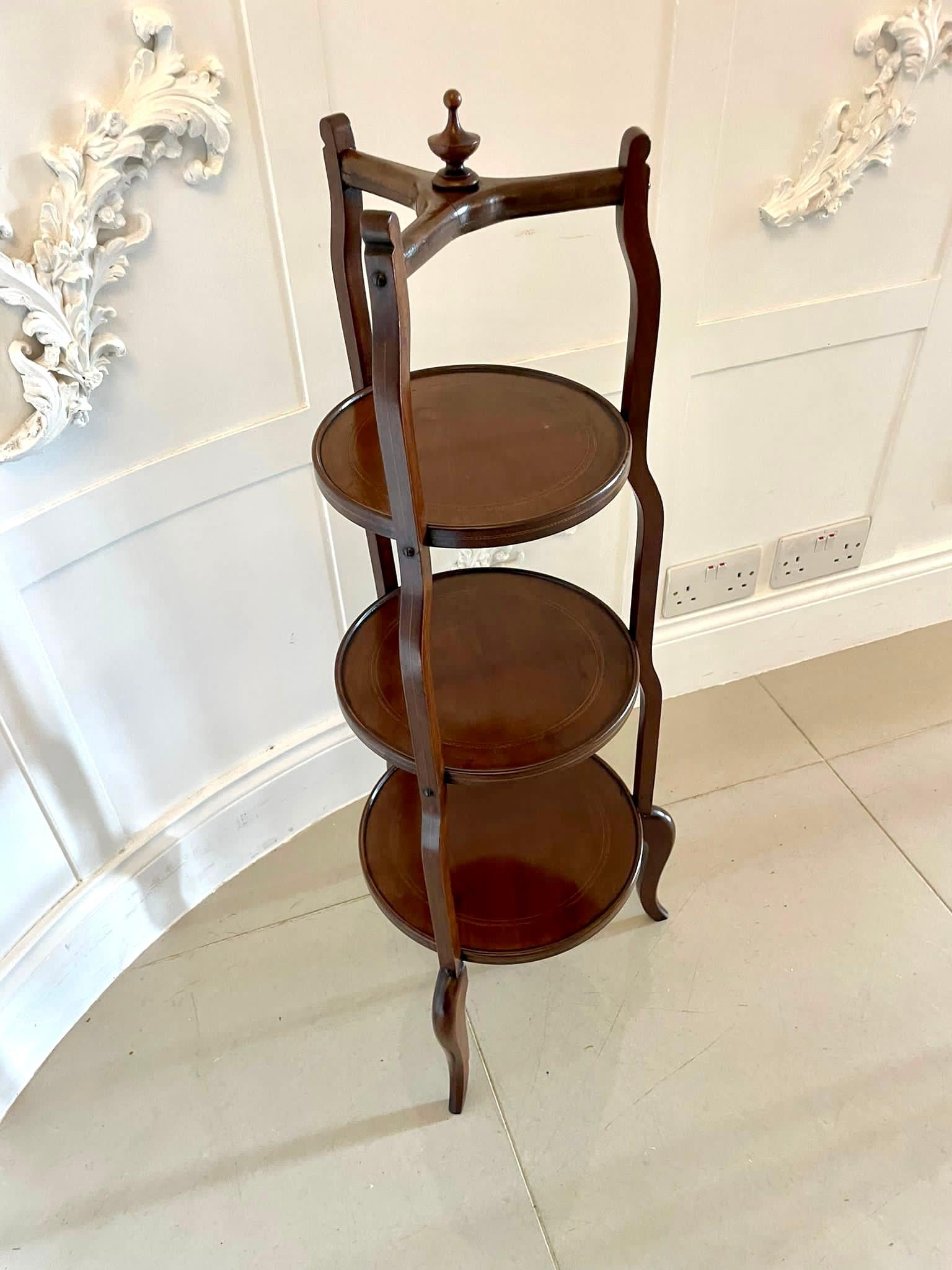 Antique Edwardian three tier cake stand with a turned finial to the top above a cross stretcher, three shaped mahogany inlaid supports united by three mahogany circular shelves with a moulded edge and raised on shaped cabriole legs.

A charming