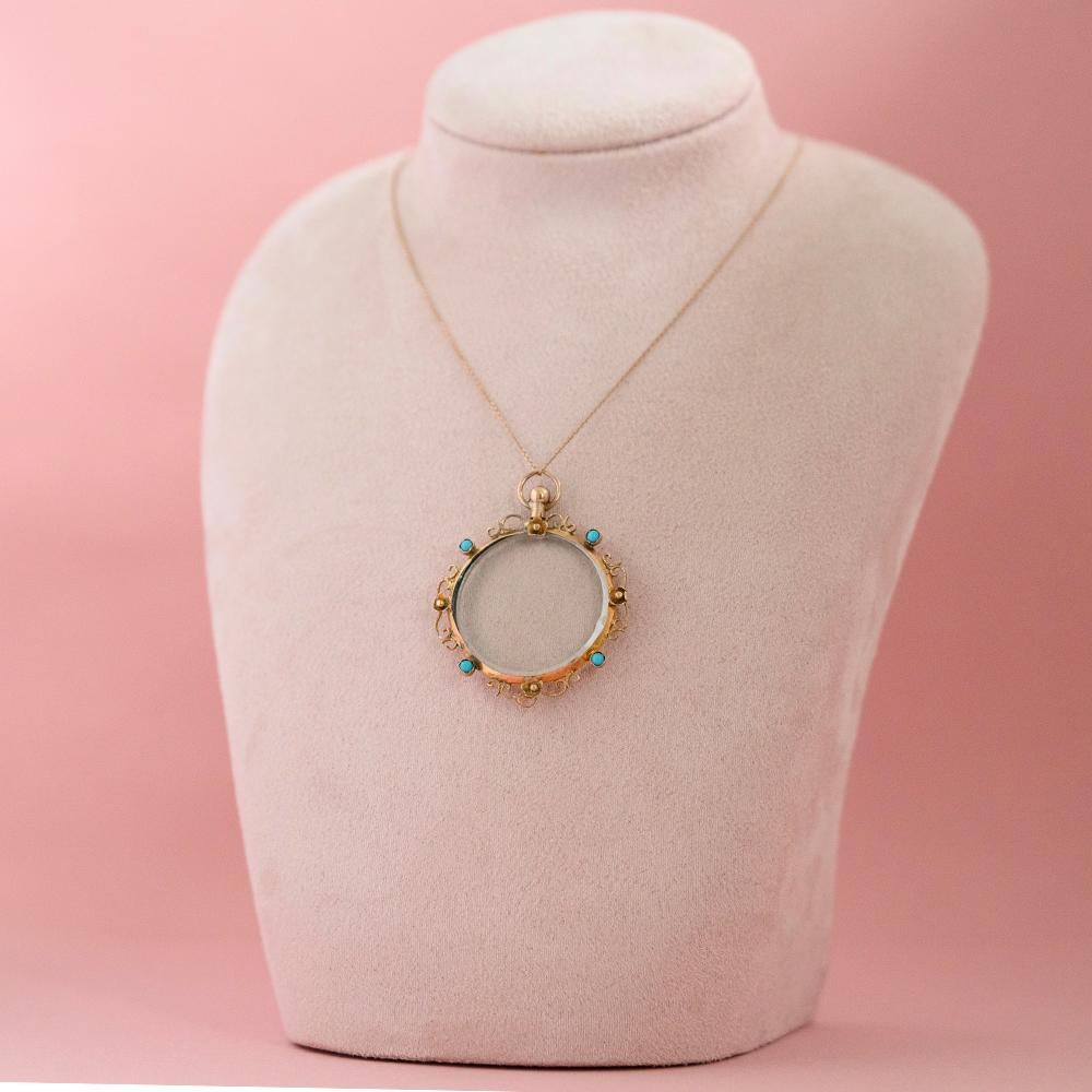 This Edwardian Turquoise Glass Locket Necklace, hallmarked in Chester in 1906, is a stunning example of early 20th-century craftsmanship. The locket features a clear glass center framed by an ornate 9ct gold halo, adorned with four vibrant turquoise