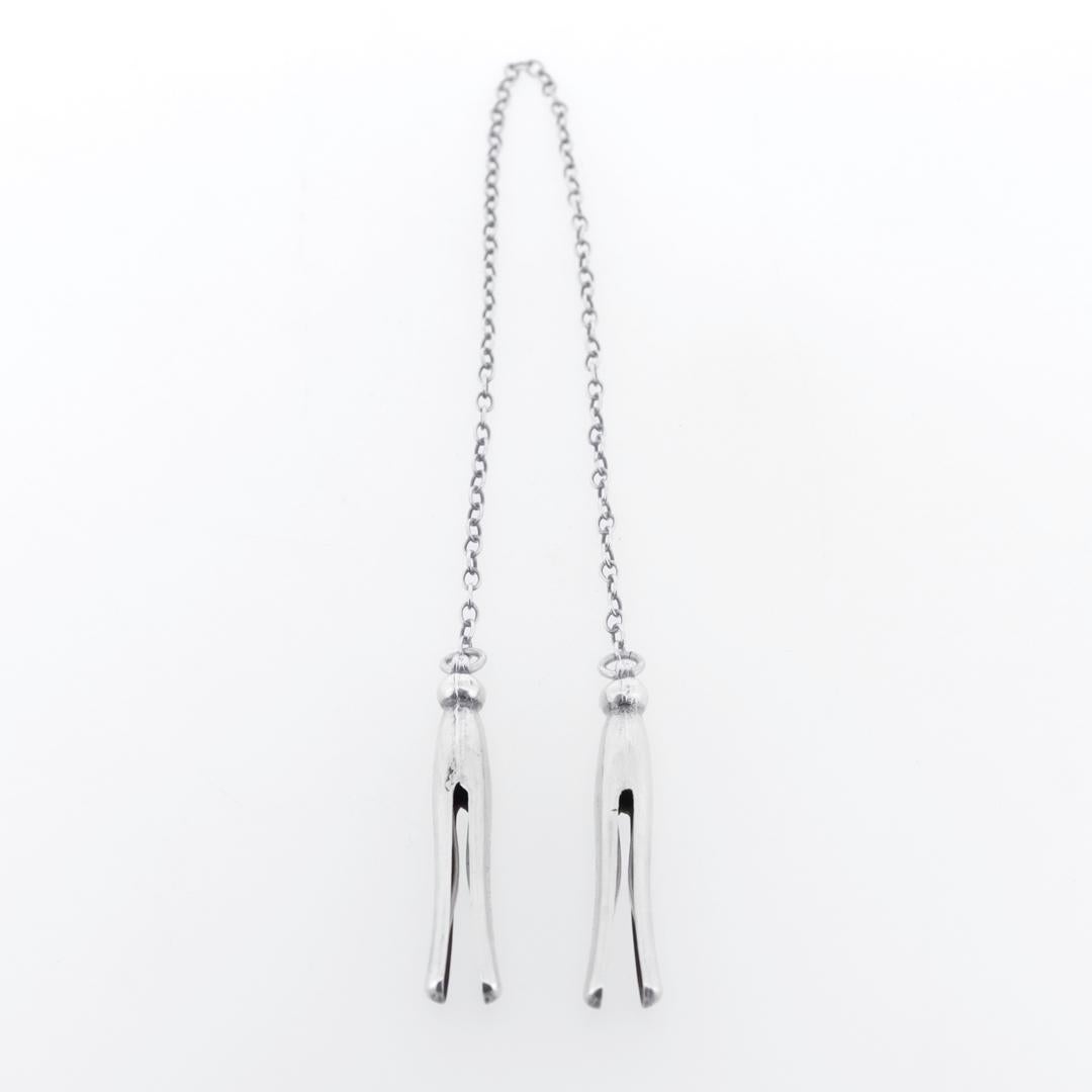 Ein feiner antiker silberner Lätzchenhalter.

Aus Sterlingsilber.

Von der Webster Co. in Attleboro, Massachusetts.

Bestehend aus zwei wäscheklammerförmigen Silberclips, die durch eine kleine Kette verbunden sind.

Markiert auf der Seite jedes
