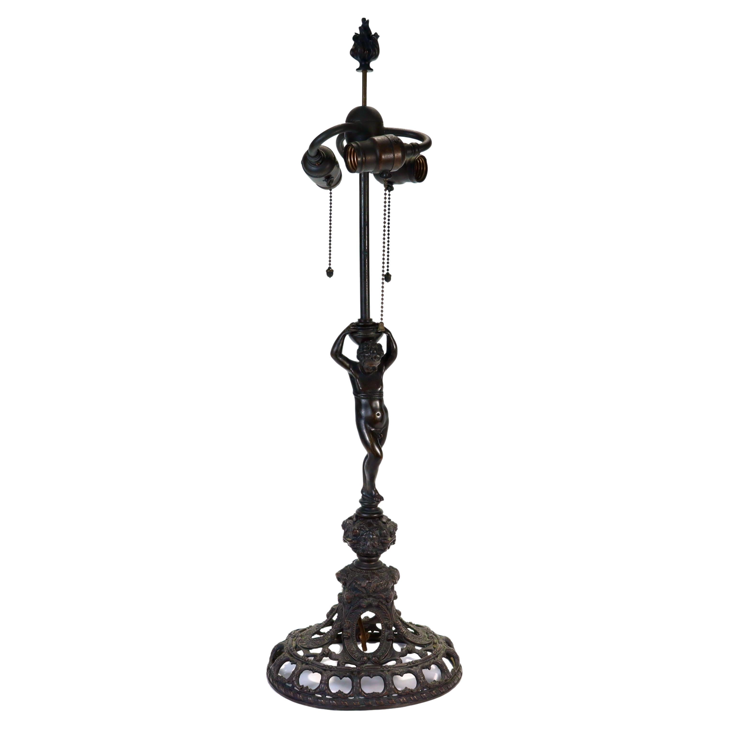 A fine Edwardian bronze table lamp.

By E.F. Caldwell.

With a pierced plunger-form base supporting a full-figured cherub pedestal & a 3-socket fixture.

With its original sockets and figural flame finial.

The surface has a dark chocolate/almost