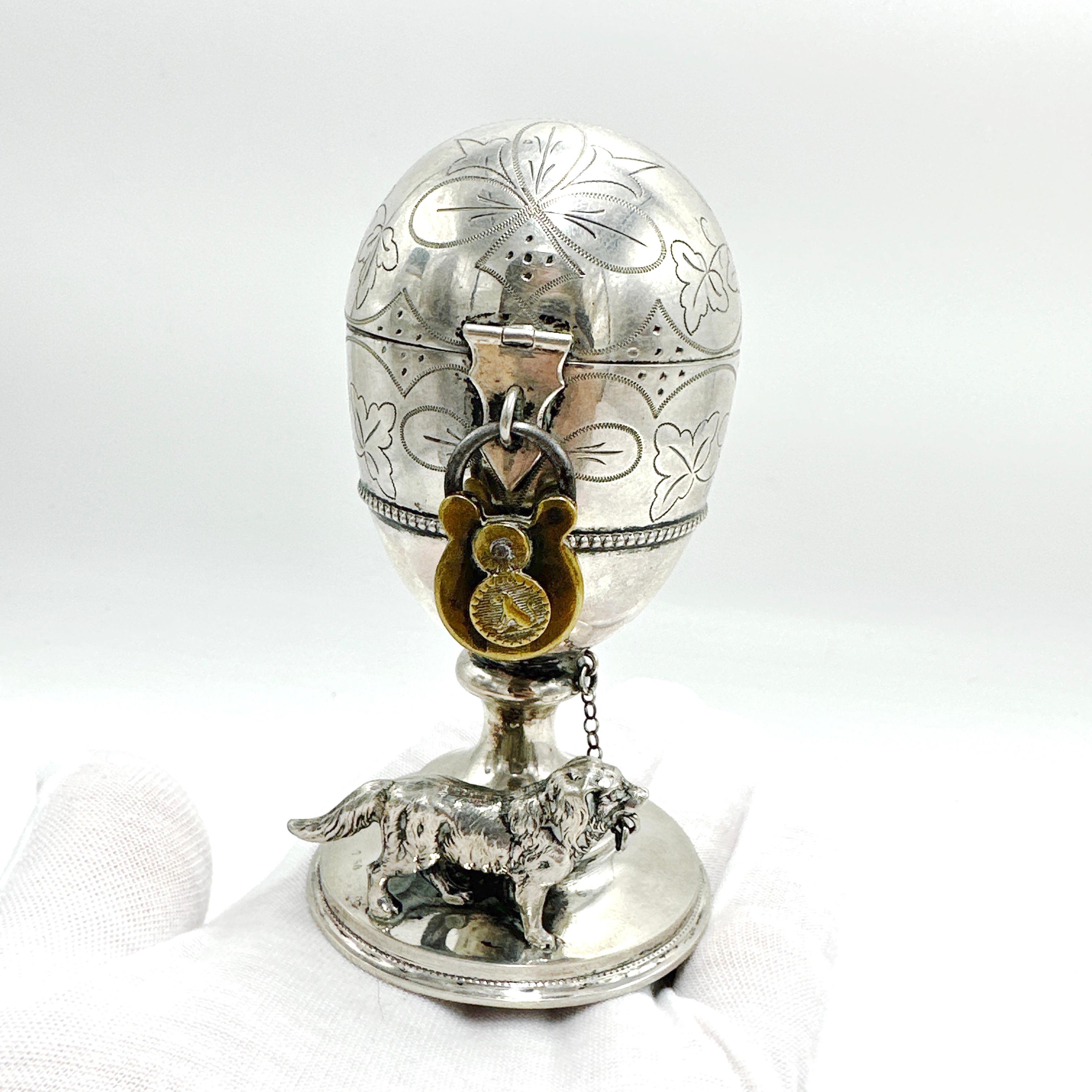 An Antique 19th century Egg Shaped 750 Silver Piggy Bank with Guard Dog and Lock. Likely American made in the Northeast, this unusual piece features an egg shaped piggy bank with a large deposit slot at the top of the egg. Secured with a brass lock