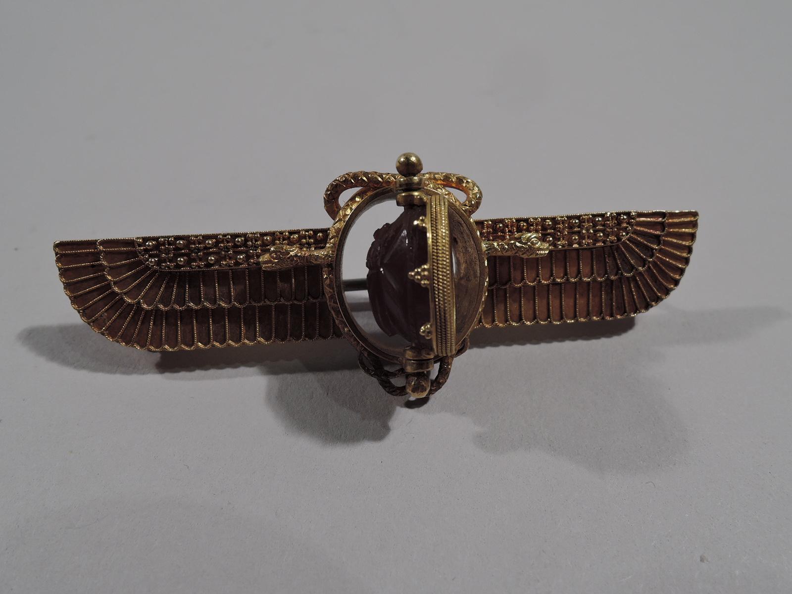 English Egyptian-Revival 18K gold brooch with scarab, ca 1870. Winged sun with fluted and stepped form. Entwined and scaly serpent forms round and open center, which supports a rotating double-sided carnelian scarab: On front is carved a beetle; on