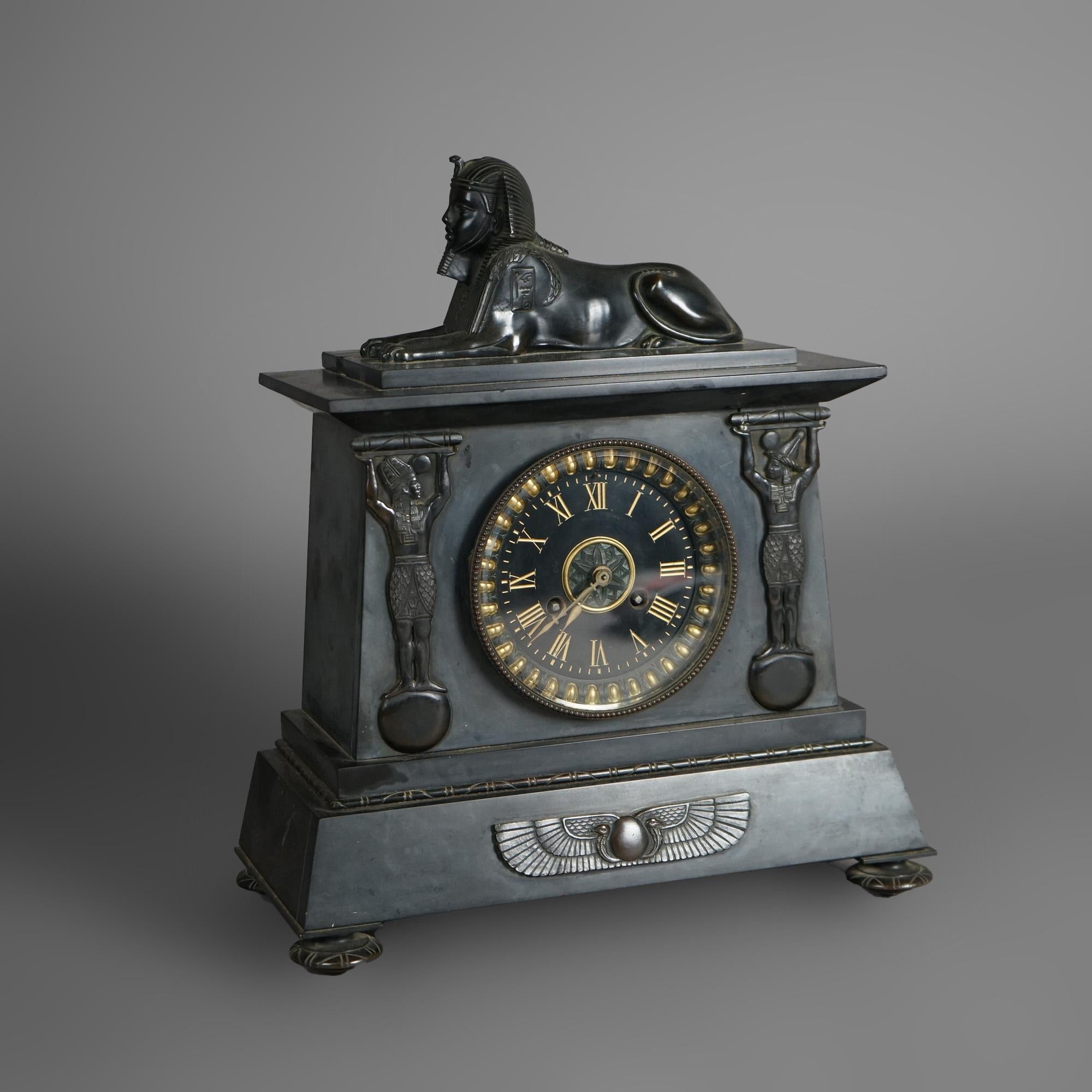 An antique Egyptian Revival figural mantel clock offers slate and bronze construction with sphinx over case having central clock face and flanking caryatides, c1880

Measures - 14.75