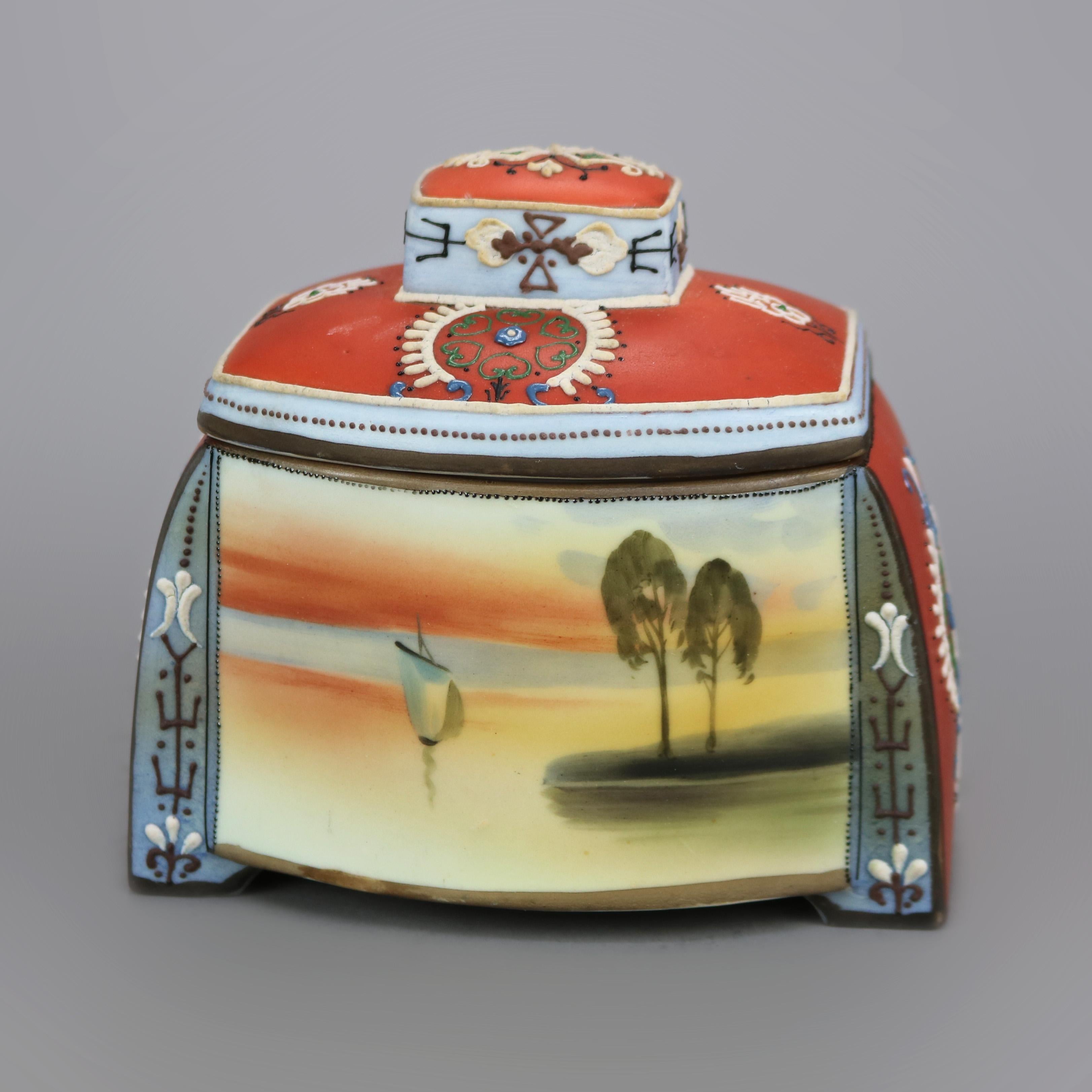 An antique Egyptian Revival Japanese Nippon scenic and footed humidor (tobacco jar) offers porcelain construction with hand painted maritime scene having harbor and junket, moriage decorated throughout with stylized tribal design, maker stamp on