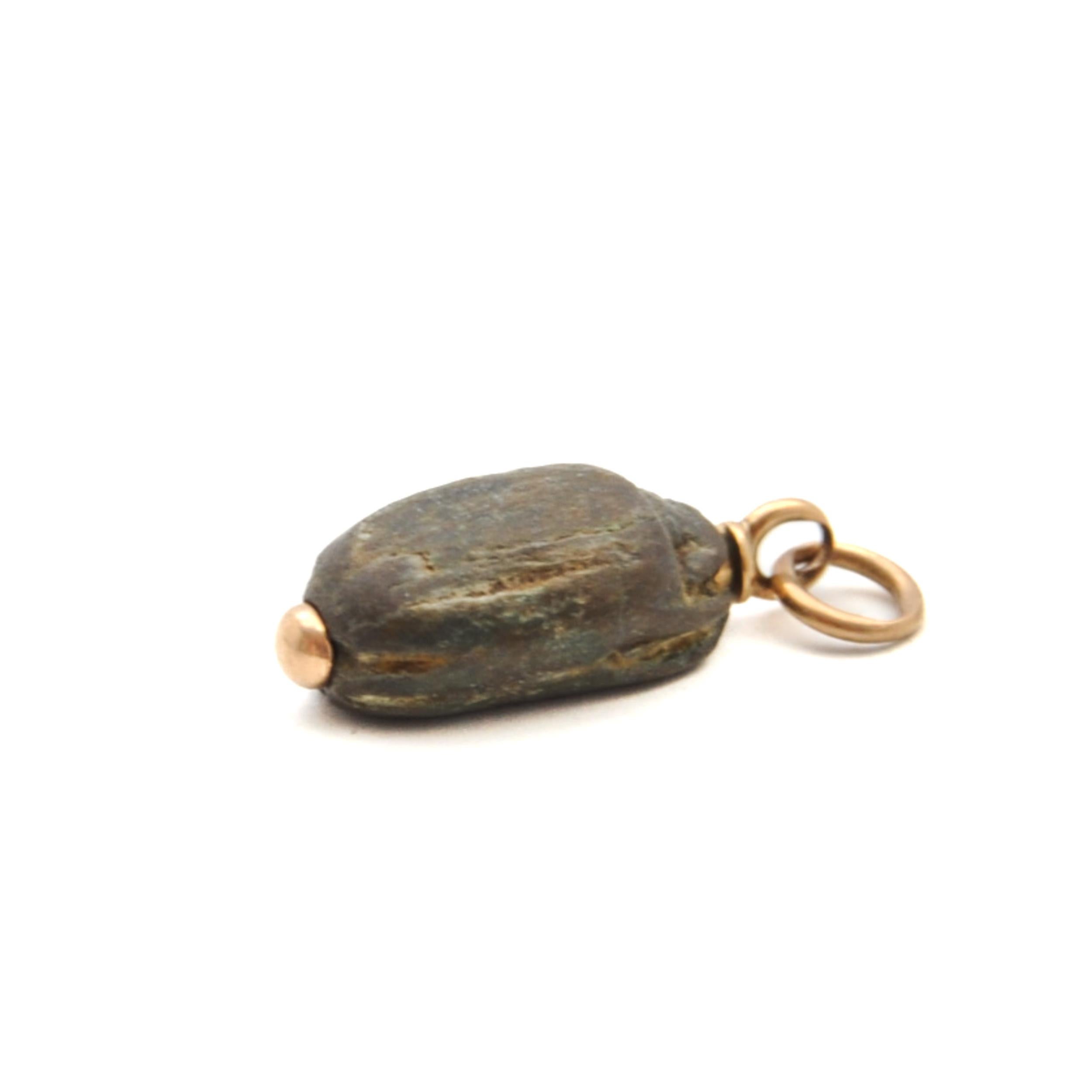 An antique Egyptian scarab charm pendant created in stone and set to a gold bail. In ancient Egypt, scarabs represented resurrection. Like the dung beetle's revolving ball, the scarab became a symbol of birth, life, death, and resurrection. Since