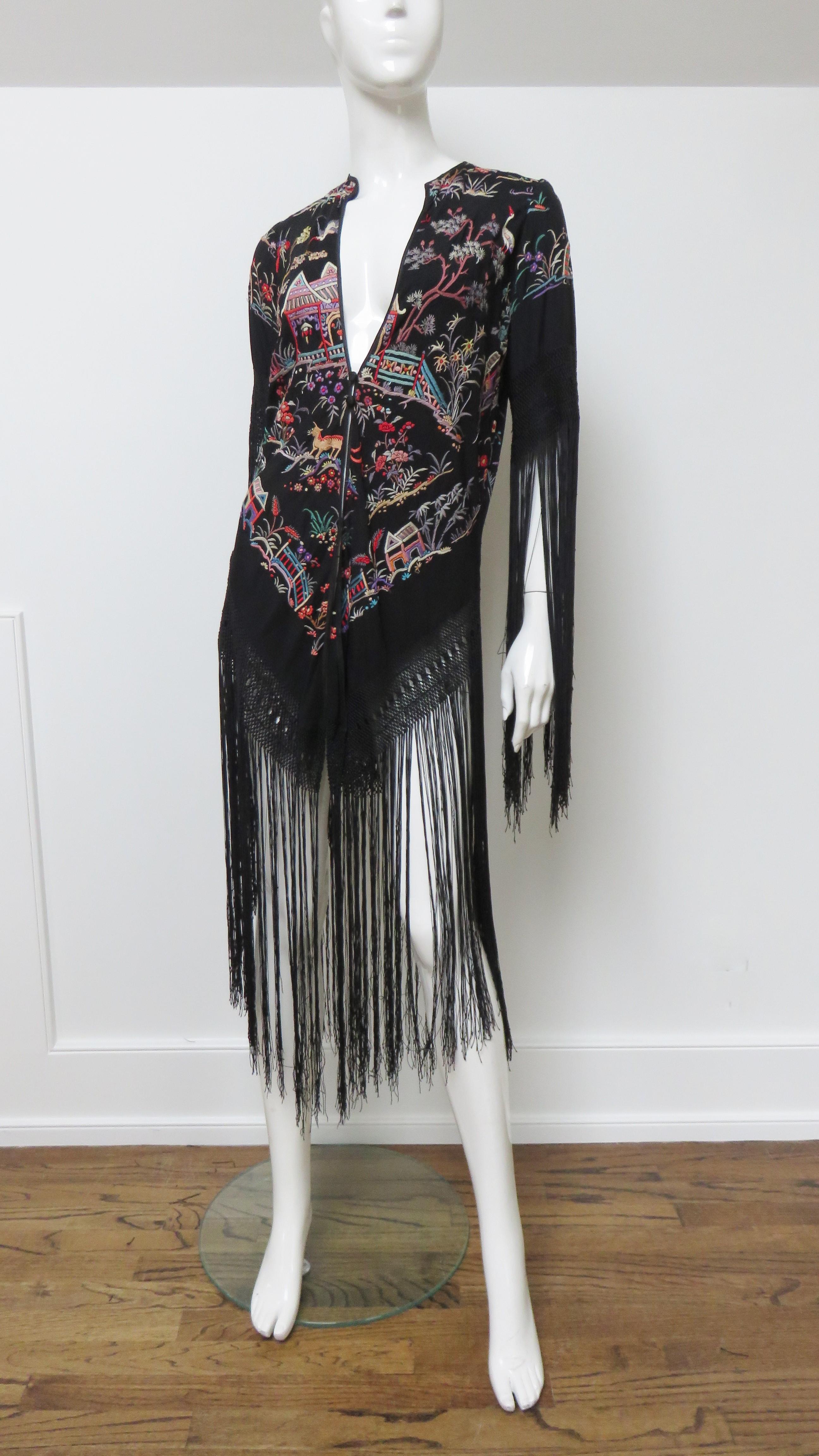 This is an elaborately embroidered 1920s black silk coat, jacket covered with gorgeous, colorful embroidery of people, birds and animals, pagodas, bridges, walkways, flowers and trees which pop against the black silk. The coat has a V neckline and