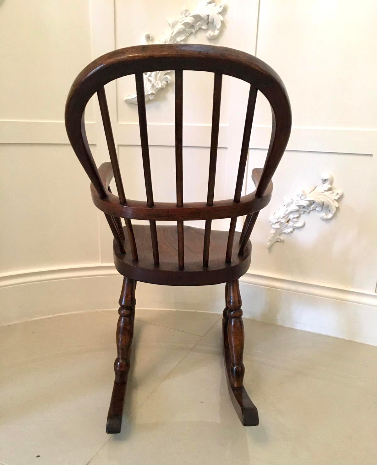 19th century antique elm and ash childs Windsor rocking chair boasting a wonderful shaped turned stick back with shaped arms supported by turned columns. The seat is crafted in solid ash and is raised on four turned legs supported on original shaped