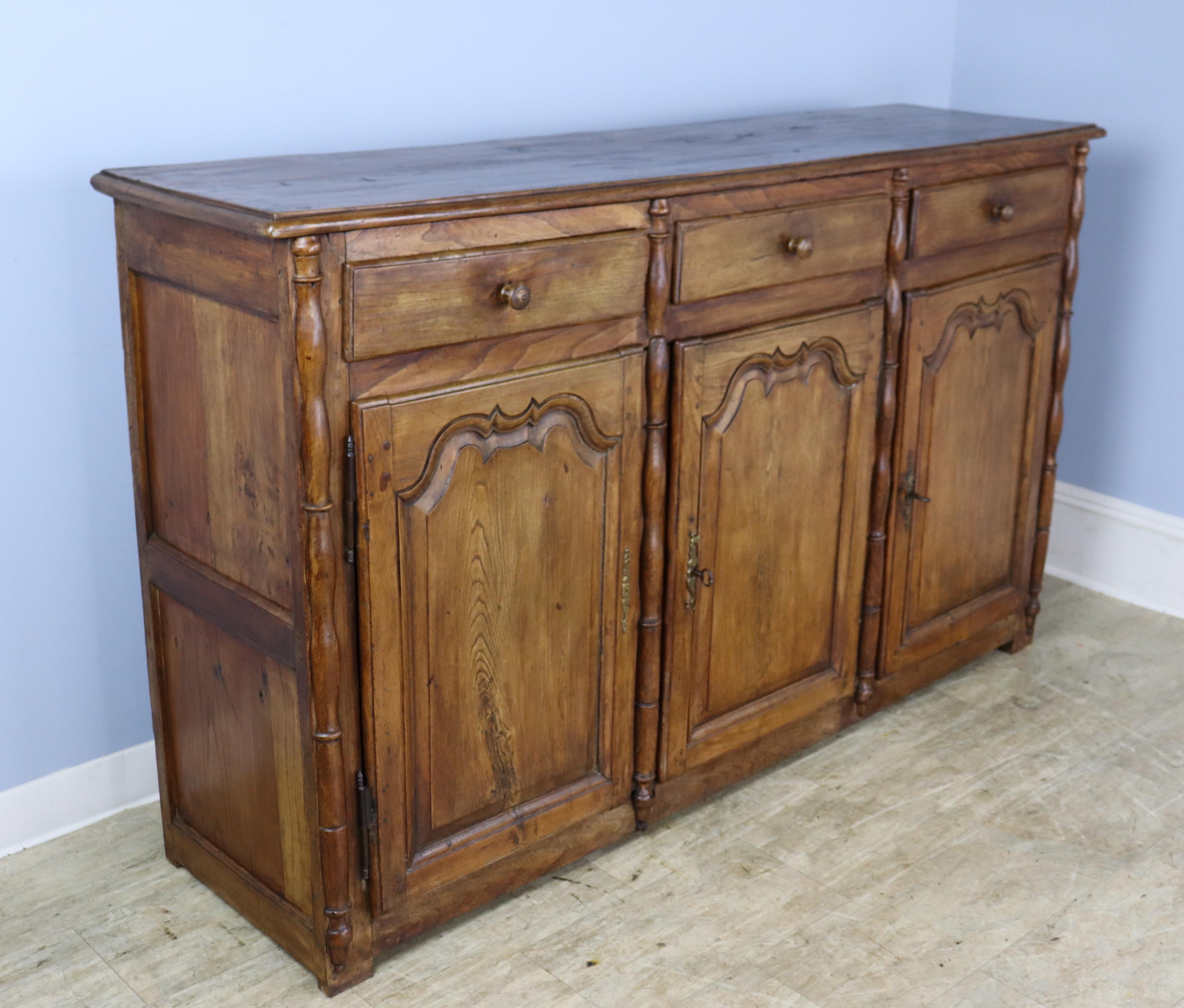 A large French chestnut buffet or enfilade, grand in both scale and sensibility. Carved detail on both the door panels and the drawers and column details to complete the look. The interior and the top are both clean and in good condition. There are