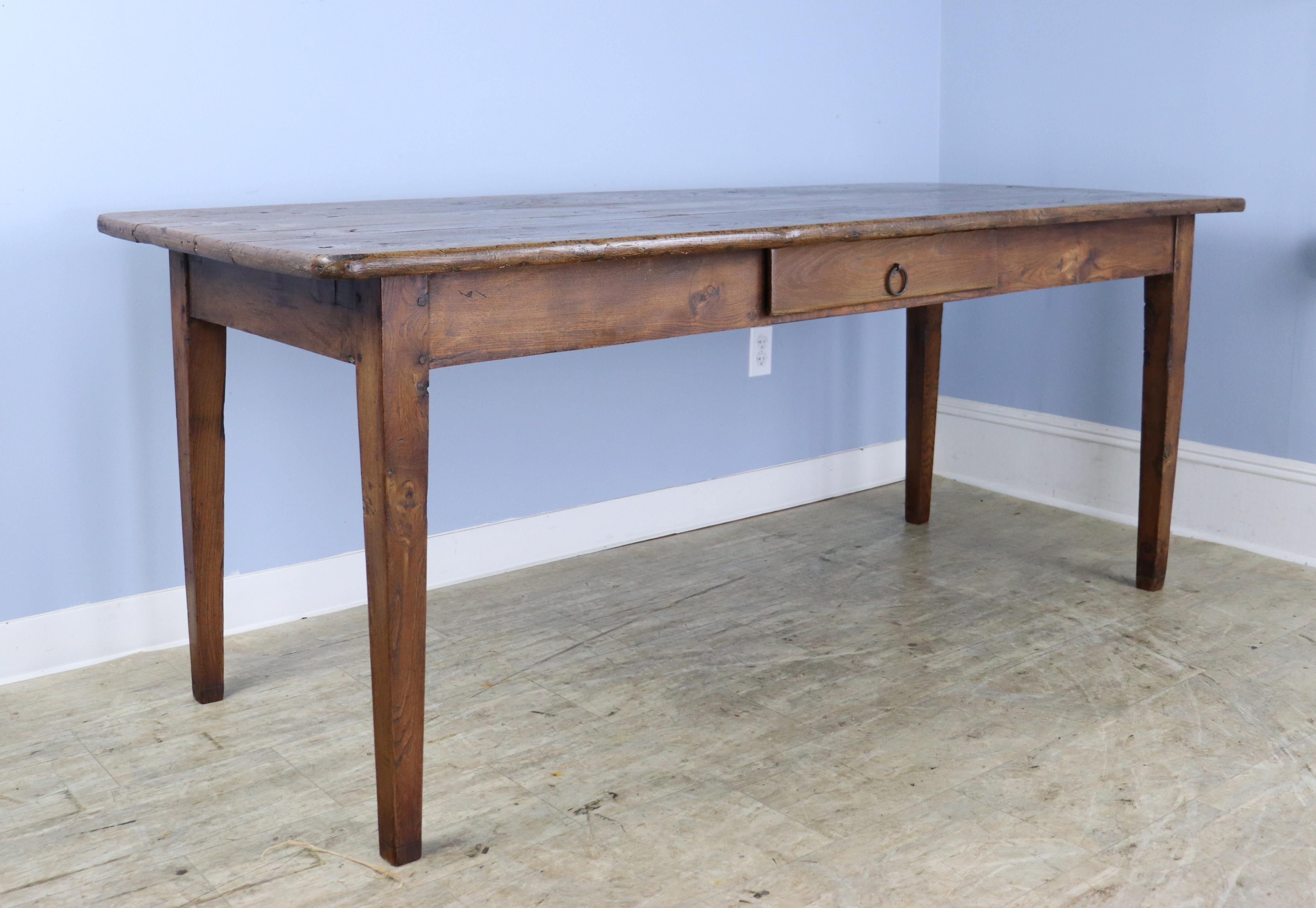 A handsome elm dining table or farm table with elegant tapered legs and a useful drawer. The top has lovely color, grain and patina. 24.5 inch apron height is good for knees and there are 64.5 inches between the legs on the long side. Nice size and