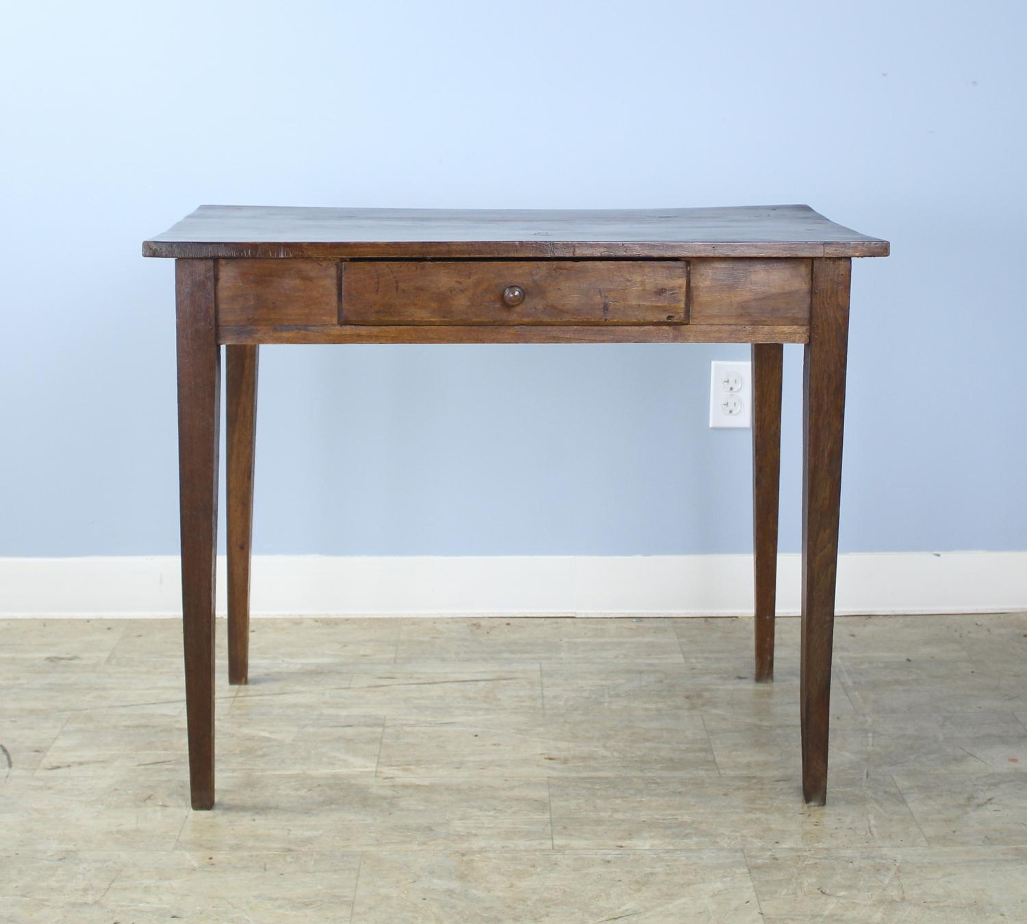 A French antique side table in dark elm with tapered legs and good graining on the top. Small single drawer adds nice detail. There is a small lift at the back of the top which does not affect the utility but is visible.
