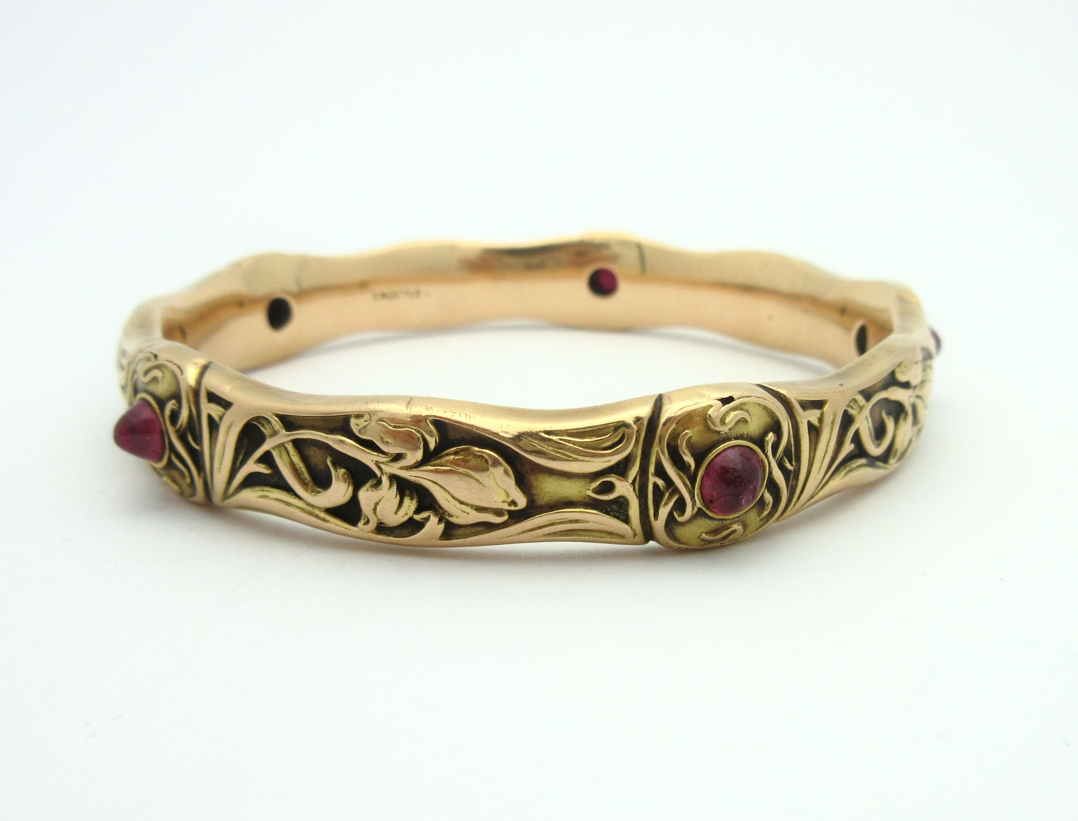 This exquisite early Art Nouveau bangle by EM Gattle & Co is a work of art.  Crafted from 14k rosy yellow gold, the floral bangle is accented by four natural unheated sugarloaf rubies and one created ruby.  The bangle features panels of repousse