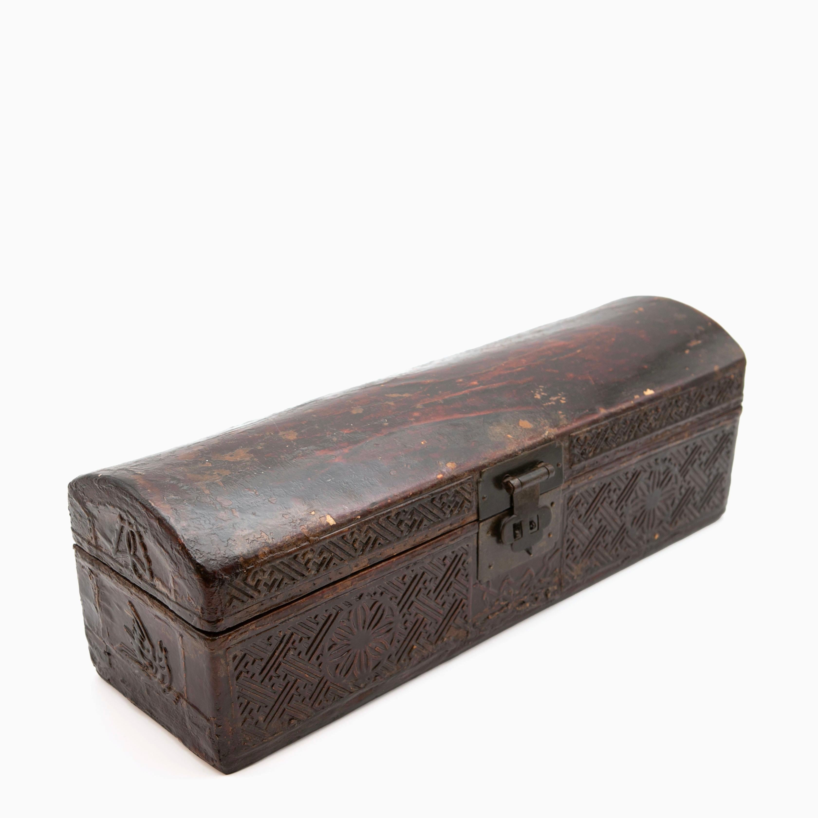 An antique Qing Dynasty pillow chest made of wood and covered with leather.
The front and sides are adorned with embossed decorations, showcasing traditional Chinese patterns.
The center of the front features patinated metal fittings.

Originally