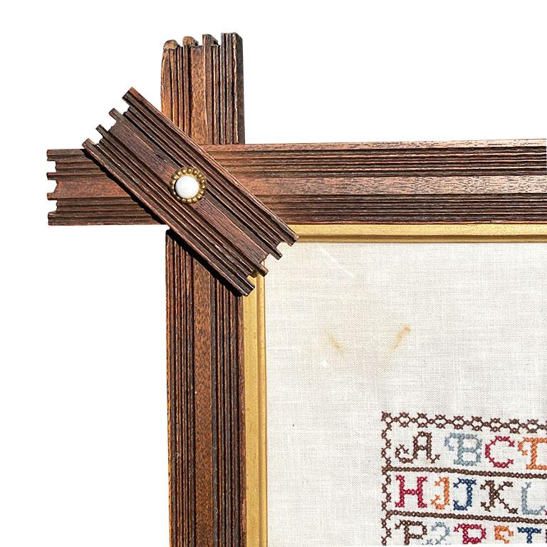 Framed in a folk art Starburst style wood frame, this embroidered sampler is a beautiful testament to the craftsmanship of artisans of the early 20th century. The frame is created from wood, with geometric carved pieces which overlap and jut out