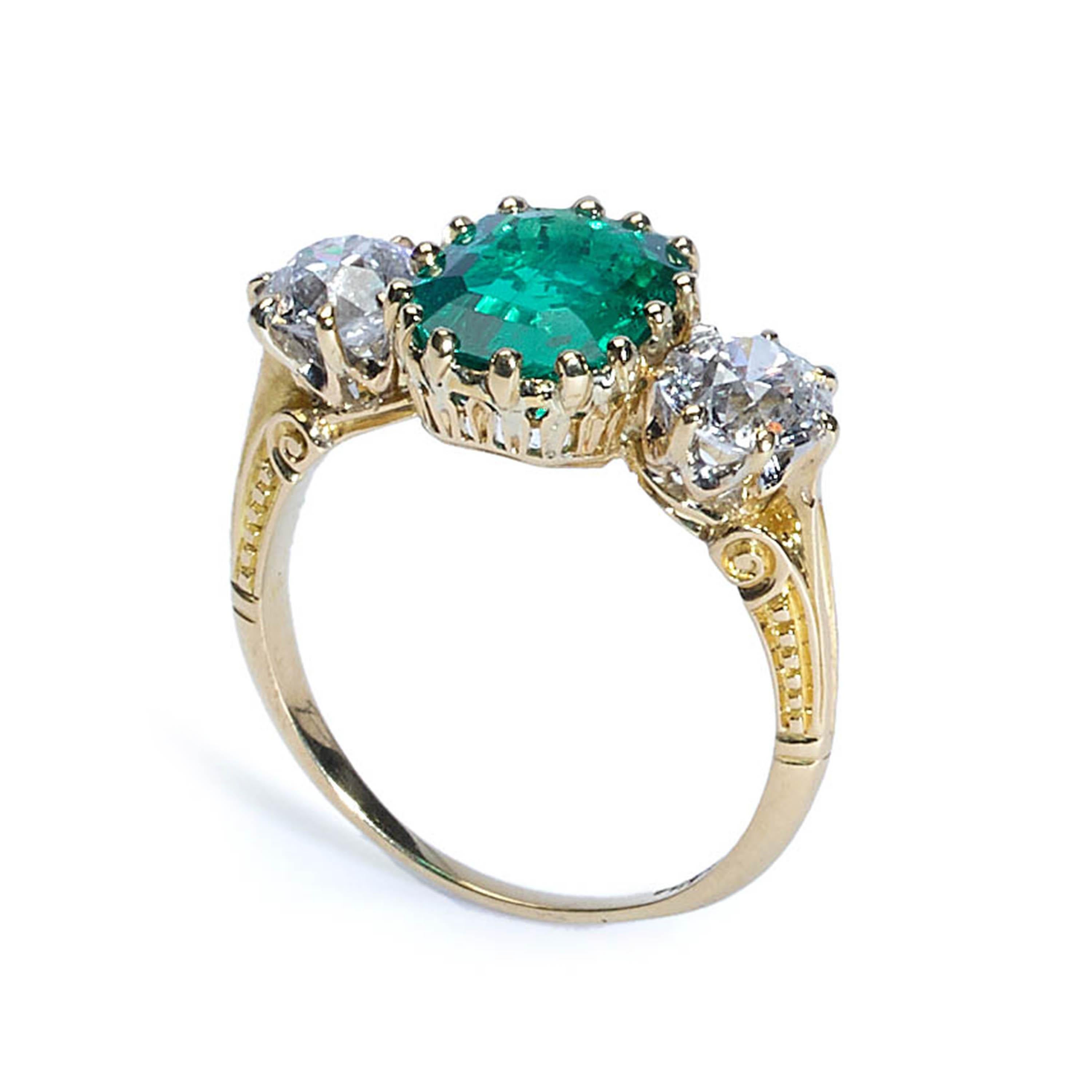 An antique emerald and diamond three stone ring, set with a Columbian emerald-cut emerald, weighing 2.66ct, in a decorative, fourteen claw setting, with two old-cut diamonds either side, weighing approximately 0.65ct, in eight claw crown settings,