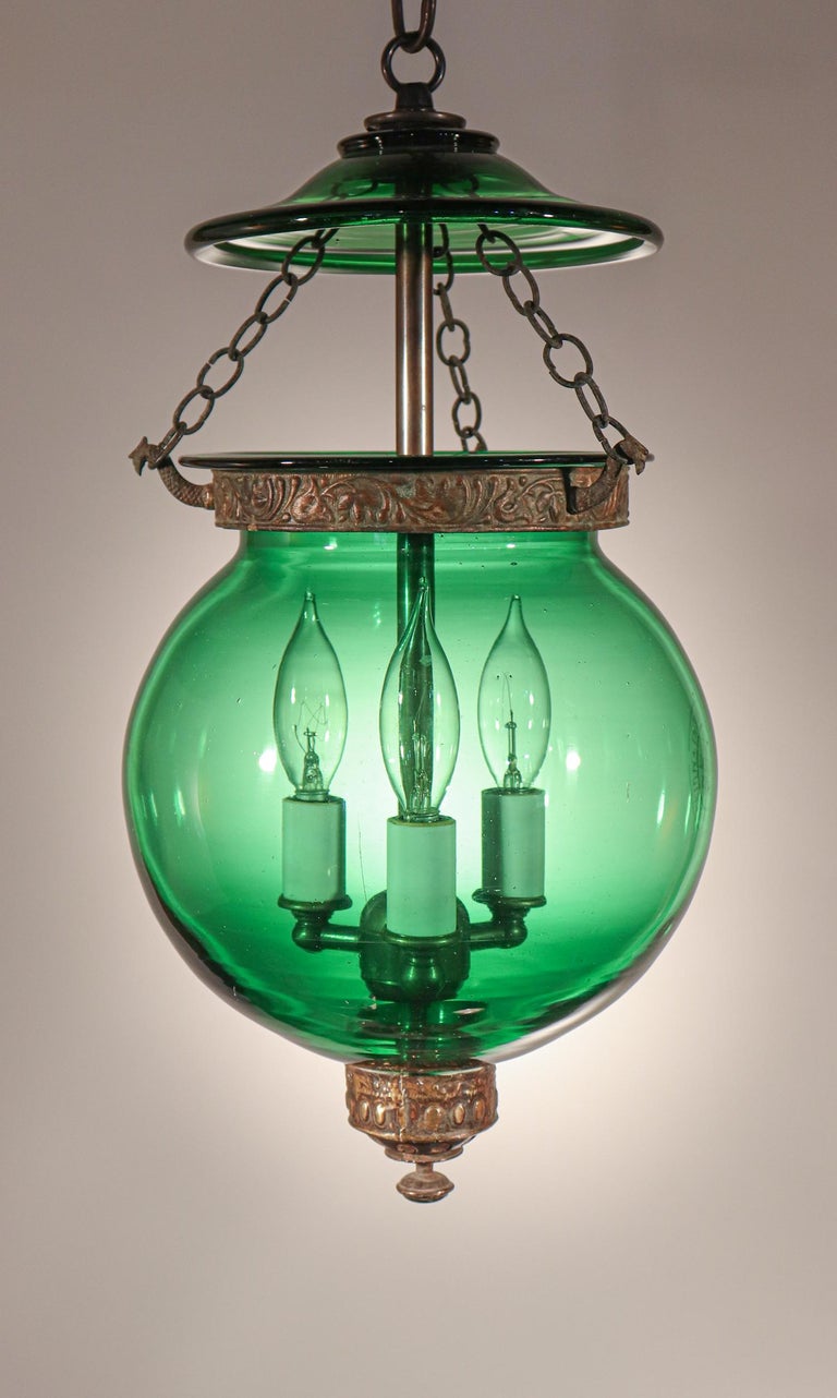 A rare and beautiful emerald-colored hand blown glass globe bell jar lantern from Belgium, circa 1890. The lantern has attractive form and features its original glass smoke bell and decorative brass finial/candle holder base, band and chains. The