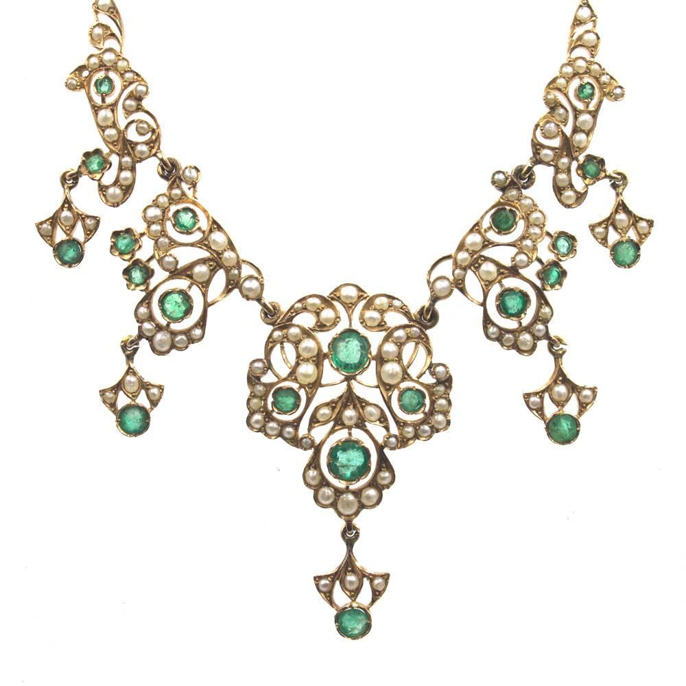 This beautifully crafted antique necklace features emerald and seed pearls set in 14 karat yellow gold. The necklace, circa late 19th Century, has a delicate open feel to it. The necklace measures 15.25 inches in length, and the emerald pearl drops