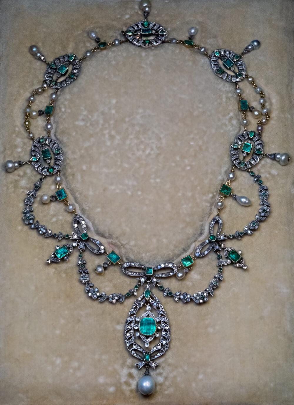 Circa 1905
The necklace is designed in the Garland style, which was fashionable in the early 1900s. It is crafted in silver-topped 18K gold (front – silver, back – gold) and embellished with emeralds, pearls, and rose cut diamonds.
The principal