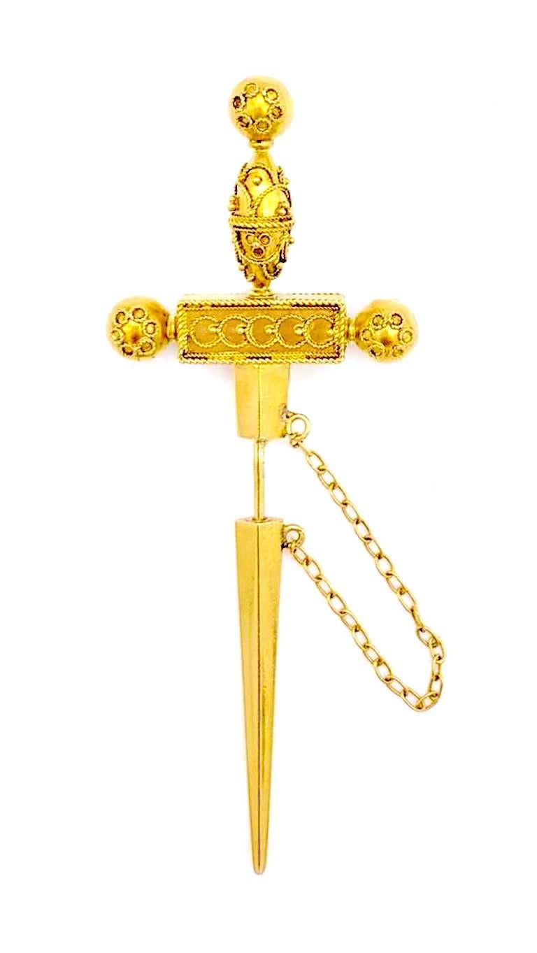 The jabbot pin is designed in the shape of a dagger, decorated with  gold granulation, applied twisted gold wire, emeralds, rubies and orient pearls.