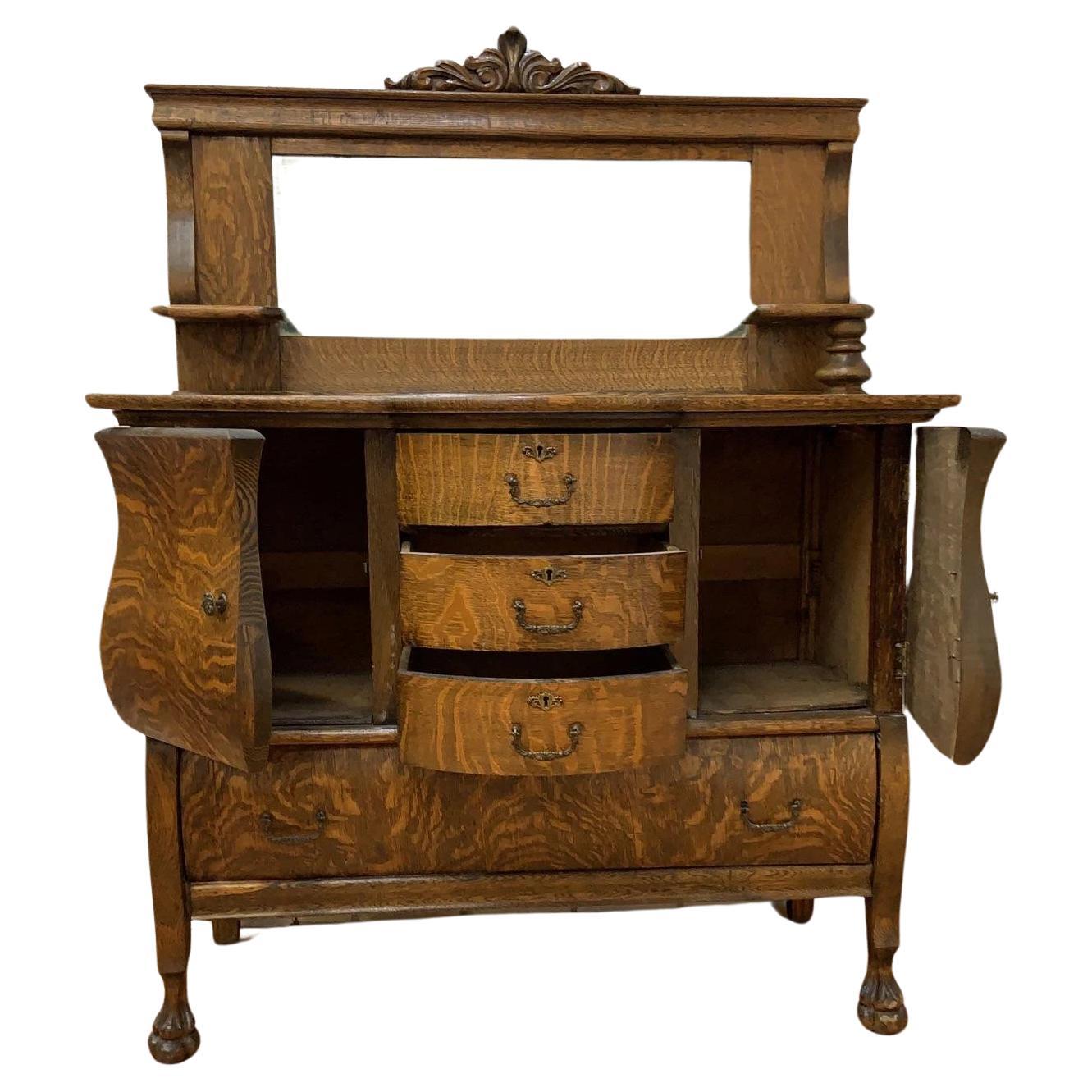 Antique Empire Antique Quarter Sawn Oak Buffet / Sideboard / Bar Cabinet with Mirror

This antique sideboard with a mirror top features a distinctive tiger oak wood grain. It features three small central drawers, one large drawer at the base, and