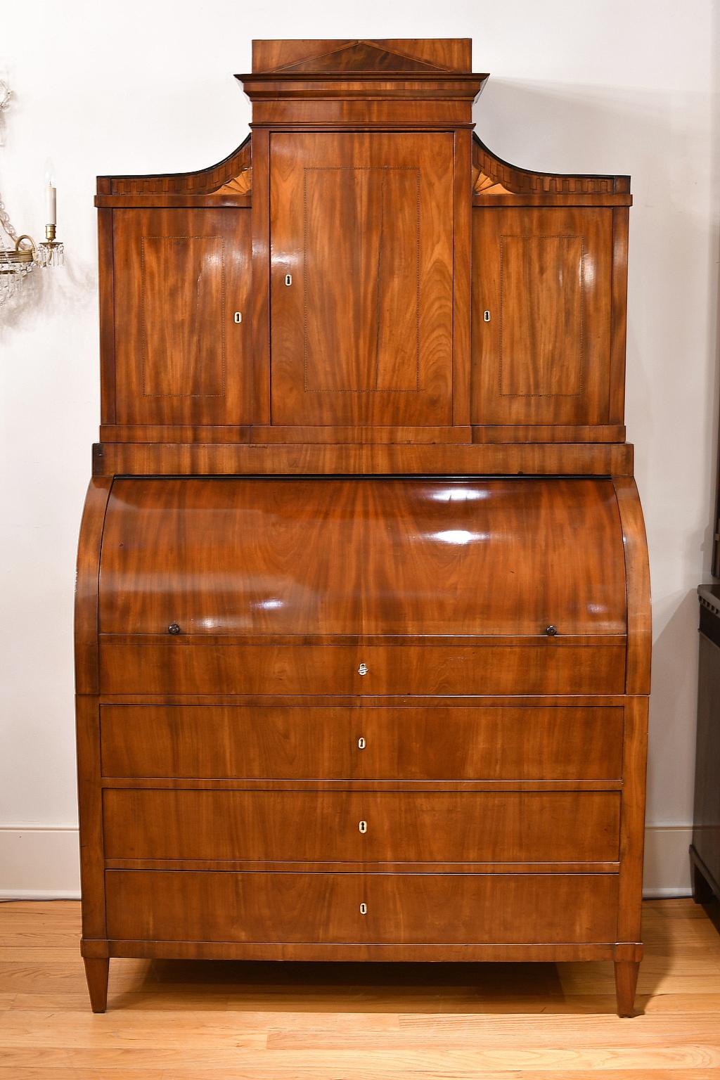 An exquisite Empire bureau secretary with bookcase, in fine West Indies/ Cuban mahogany. Denmark, circa 1800. Cylinder top opens to a pull-out desk which offers an adjustable lectern or writing surface that is flanked by sliding storage