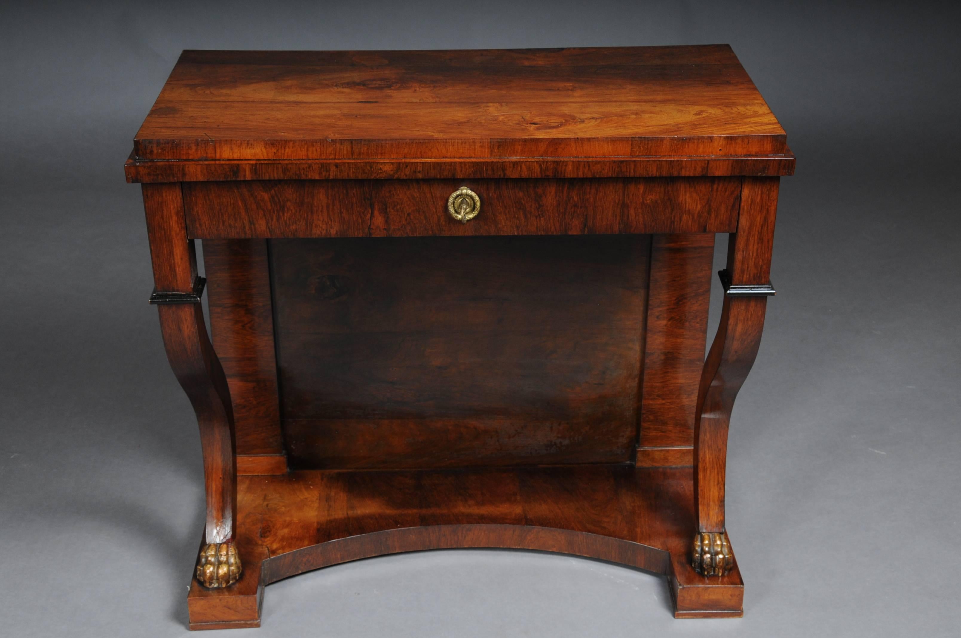 Solid wood with veneer, partly gilded. Rectangular cover plate with an inconspicuous frame and S-shaped curly supports on carved claws, which are held in gold. The base is arched. Partially ebonised. Lockable drawer with key.

(E-22).