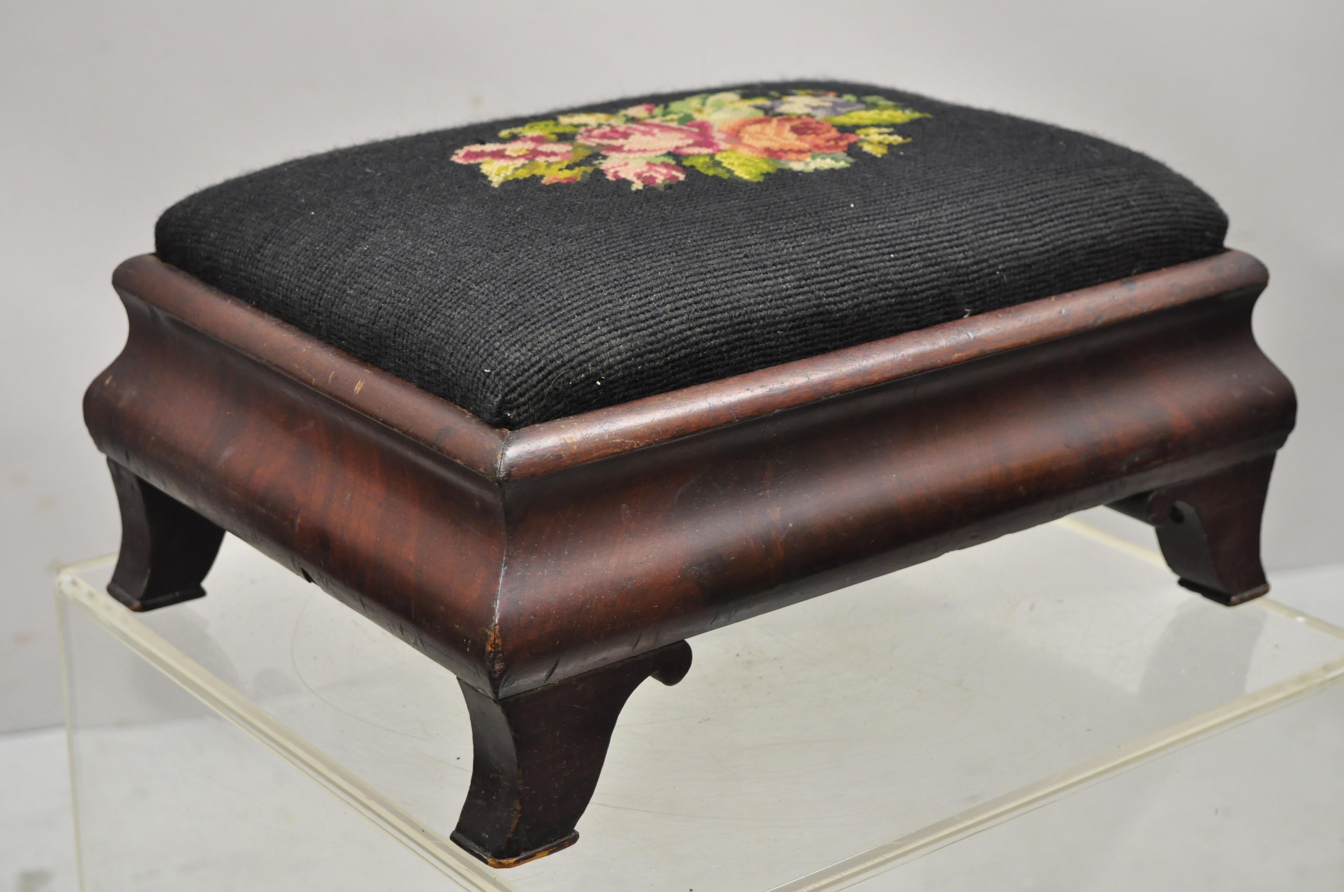 Antique Empire Crotch Mahogany Black Needlepoint small ottoman footstool. Item features black needlepoint seat with flower design, beautiful wood grain, shapely saber legs, very nice antique item, great style and form. Circa 19th Century.