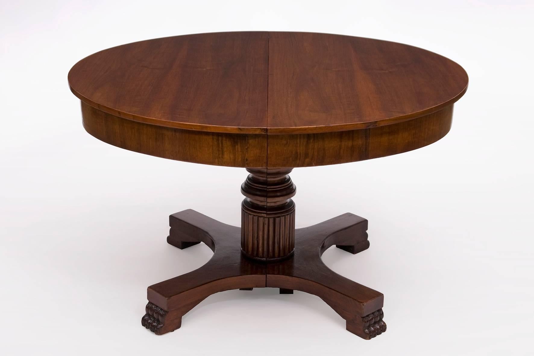 An antique Empire extension table standing on an quadruple middle foot with paw feet and with the top veneered in walnut. The foot is divisible in the middle. When the table is pulled apart, a hidden support leg reveals and supports the main foot