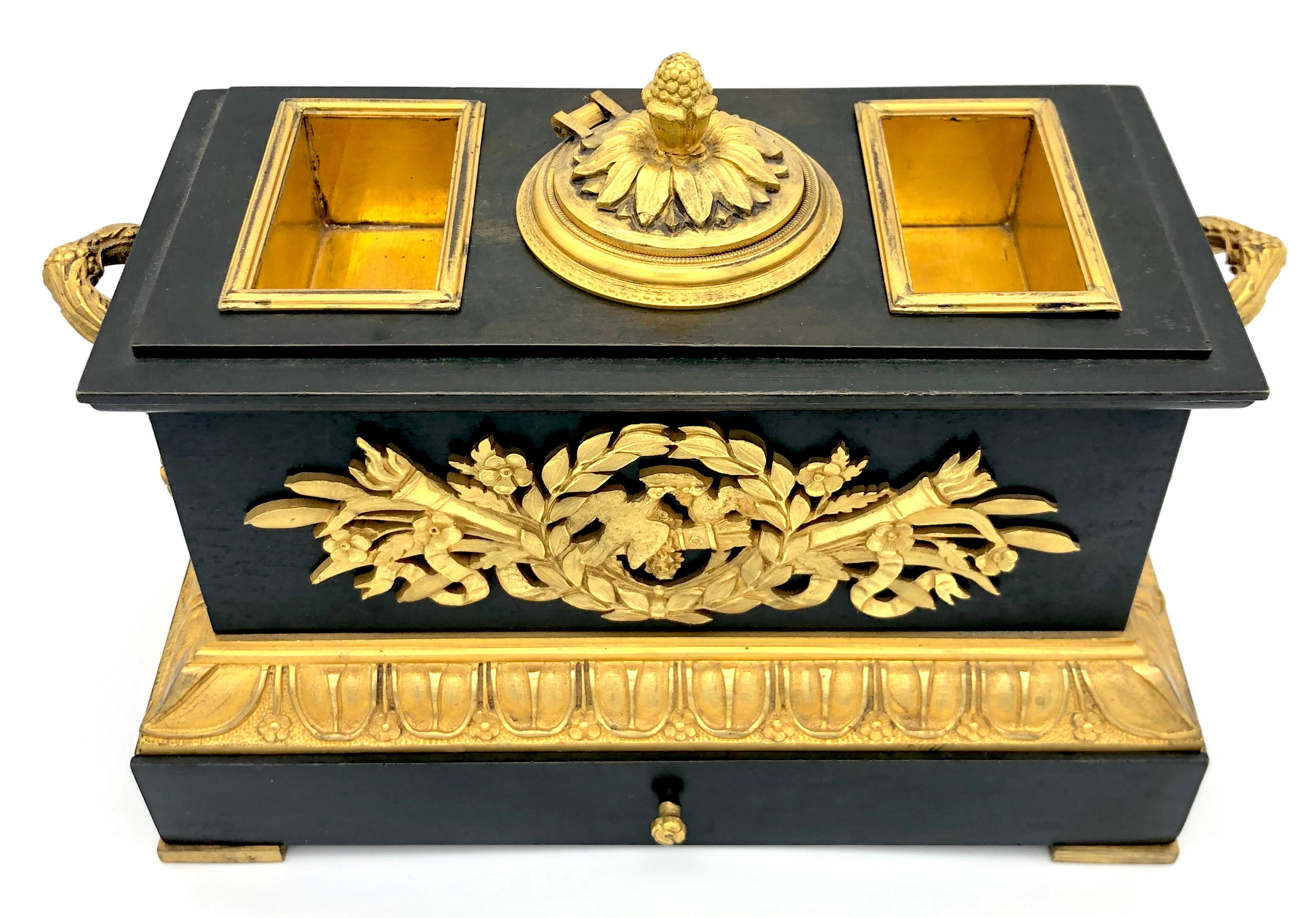 Excepional patinated bronze inkstand in the shape of a cascet on a pedestal with a drawer. It has exquisitely cast ormolu applications depicting lovers symbolic within a wreth, i.e. torches, doves, arrows in their quiver, but also flowers, leaves