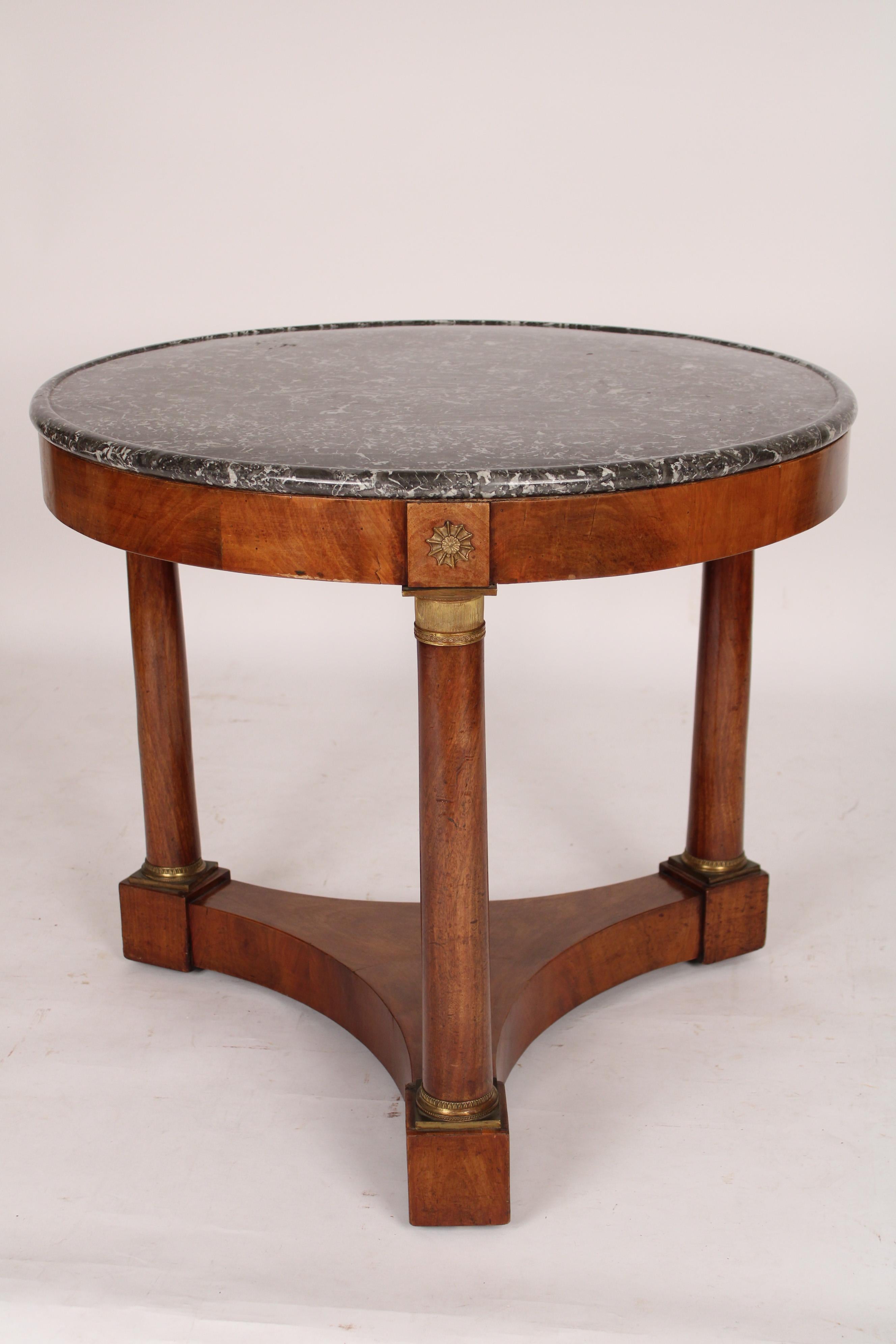 Antique Empire style mahogany center table with marble top, 19th century. With a grey and white marble top with grooved rim, flame mahogany frieze, columns with gilt bronze mounts resting on a mahogany base.