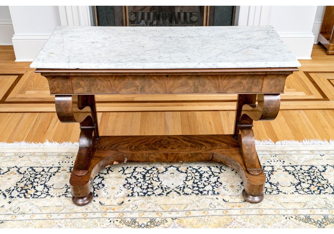 A fabulous antique Empire style marble top, mahogany veneered pier table, features a single drawer. The whole is raised on four cushion form feet with trestle style support.  Fabulous scroll supports flank either side of the drawer which features a
