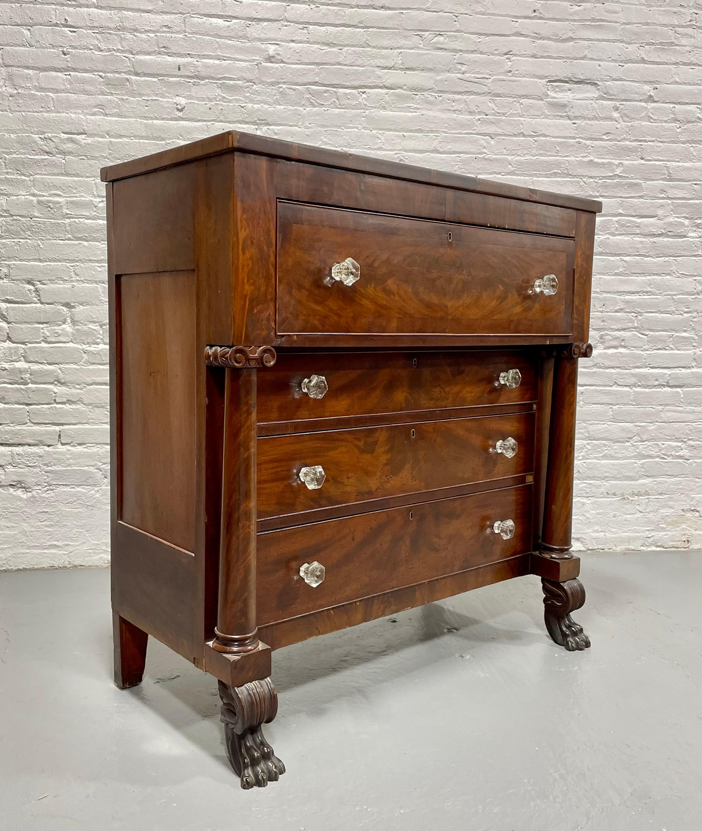 Antique figured Mahogany Empire Chest of Drawers featuring original glass pulls, full columns and hand cut dovetailed drawers. The four large drawers are flanked by elegant rounded columns topped with carved accents and raised on clawfoot front