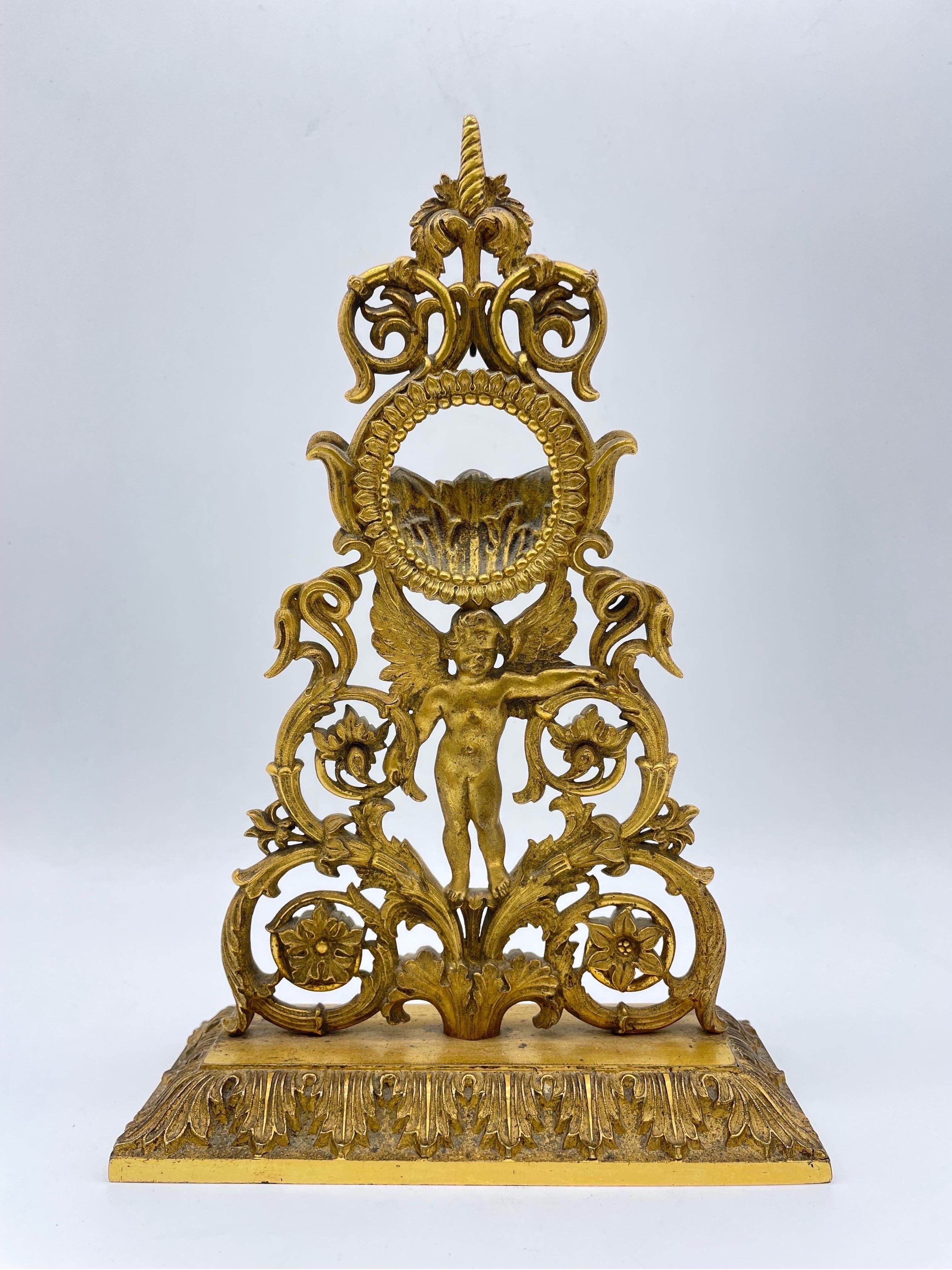 Antique Empire Porte Montre/pocket watch stand around 1800

Base decorated with acanthus leaves. Tapered bronze decorations, a putto in the middle with a round shape/frame for a pocket watch

Solid bronze, fire-gilded,
Paris around 1805-1815

Very
