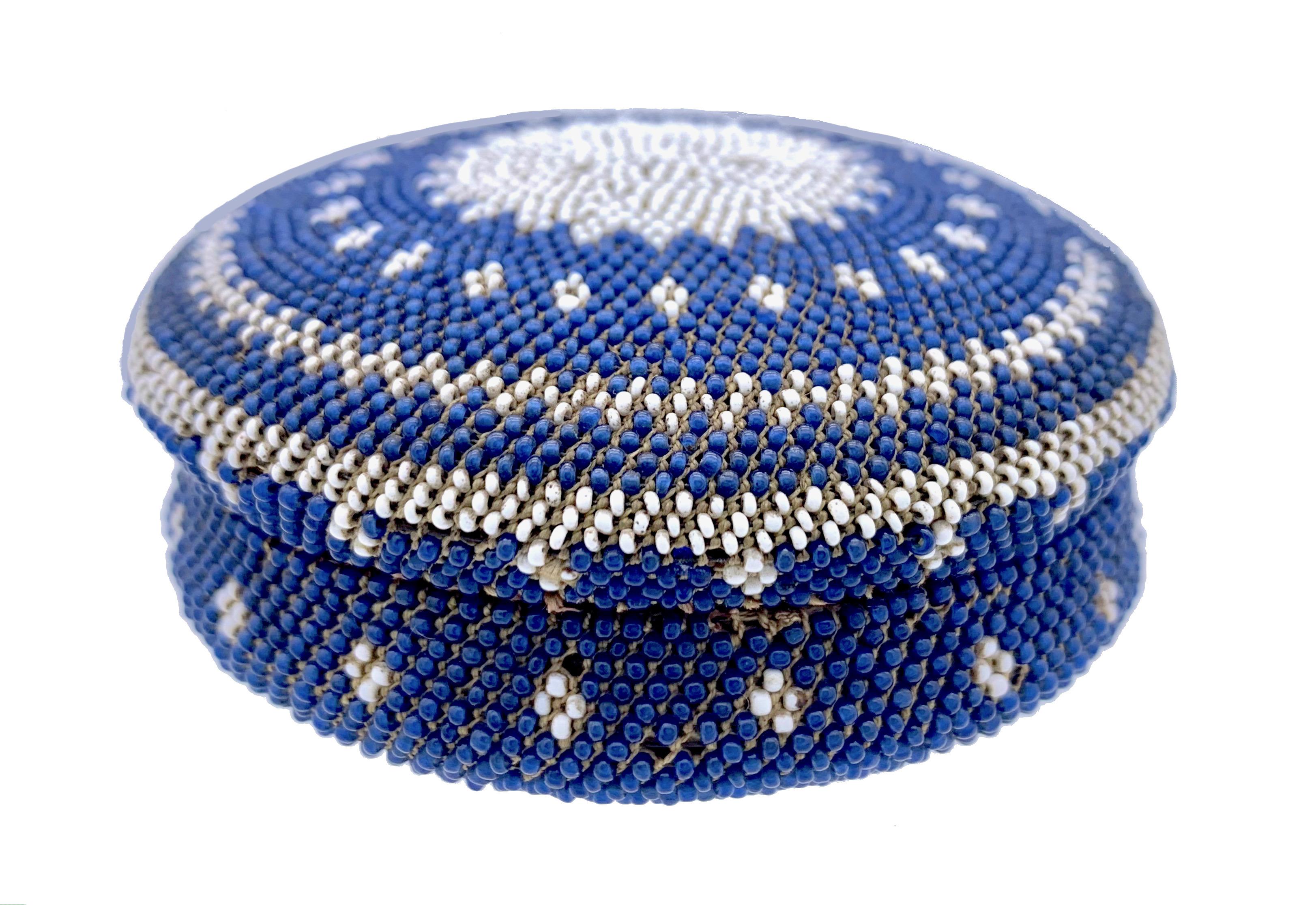 This delicate snuffbox has been made out of pressed horn and is covered entirely in blue and white glass beads threaded on cotton string. The lid is decorated with a sun emblem, a lozenge and a zigzag pattern and the French words DON DAMITIE, gift