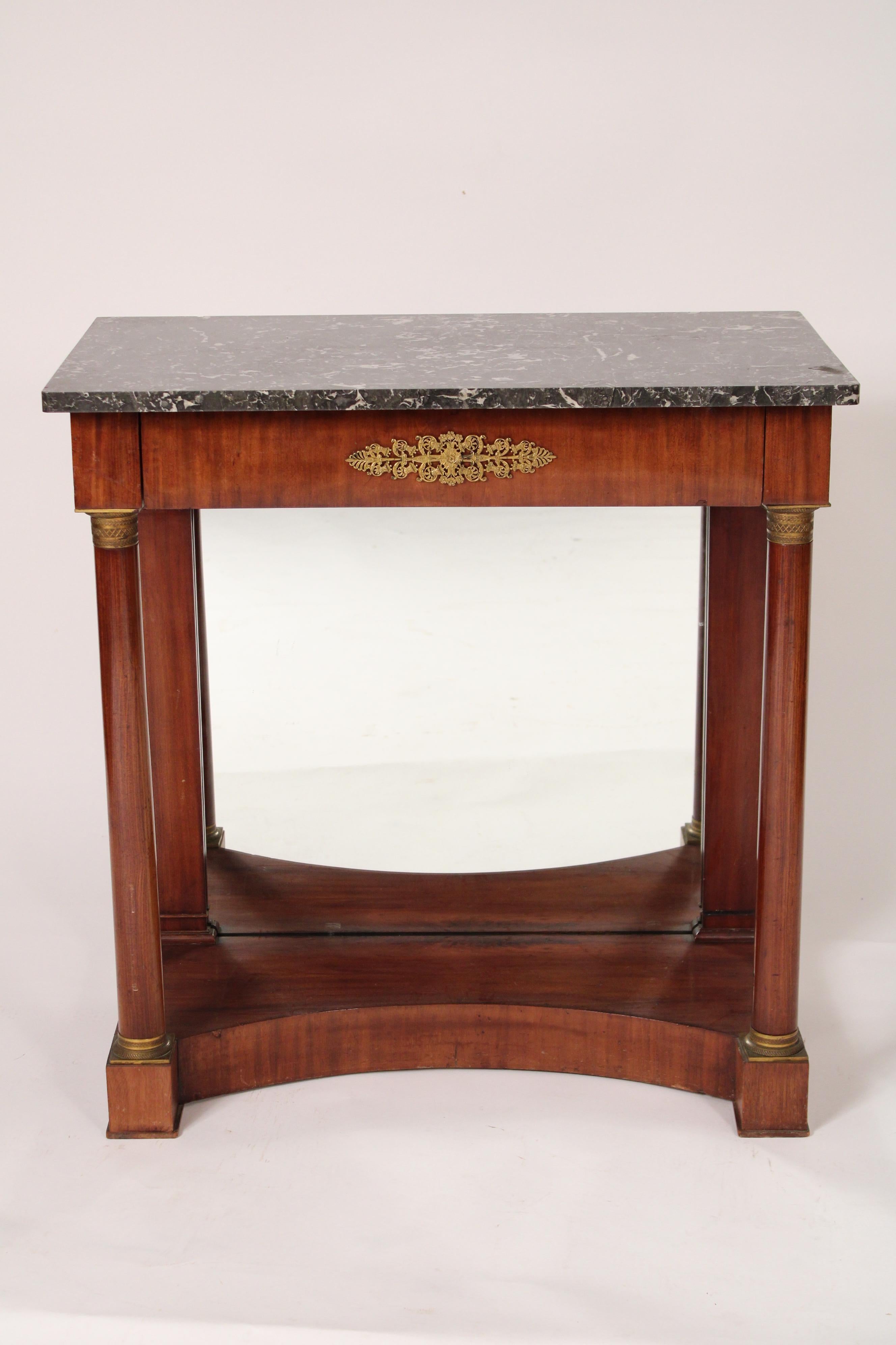 Antique Empire style mahogany console table with a marble top, circa 1900. With a rectangular grey and white marble top with slightly rounded front corners, a frieze drawer with a well chased brass plaque with bells and flowers, two columns with